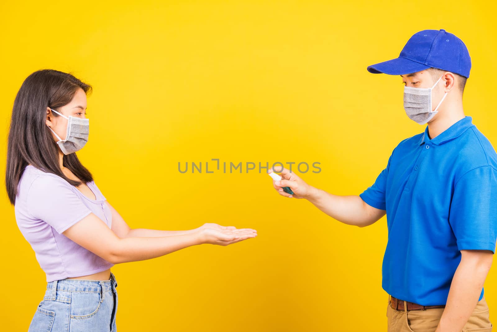 Family man applying hand spraying alcohol spray sanitizer clean and disinfect woman hands both wearing face mask protective, Protection Covid-19 coronavirus outbreak, isolated on yellow background