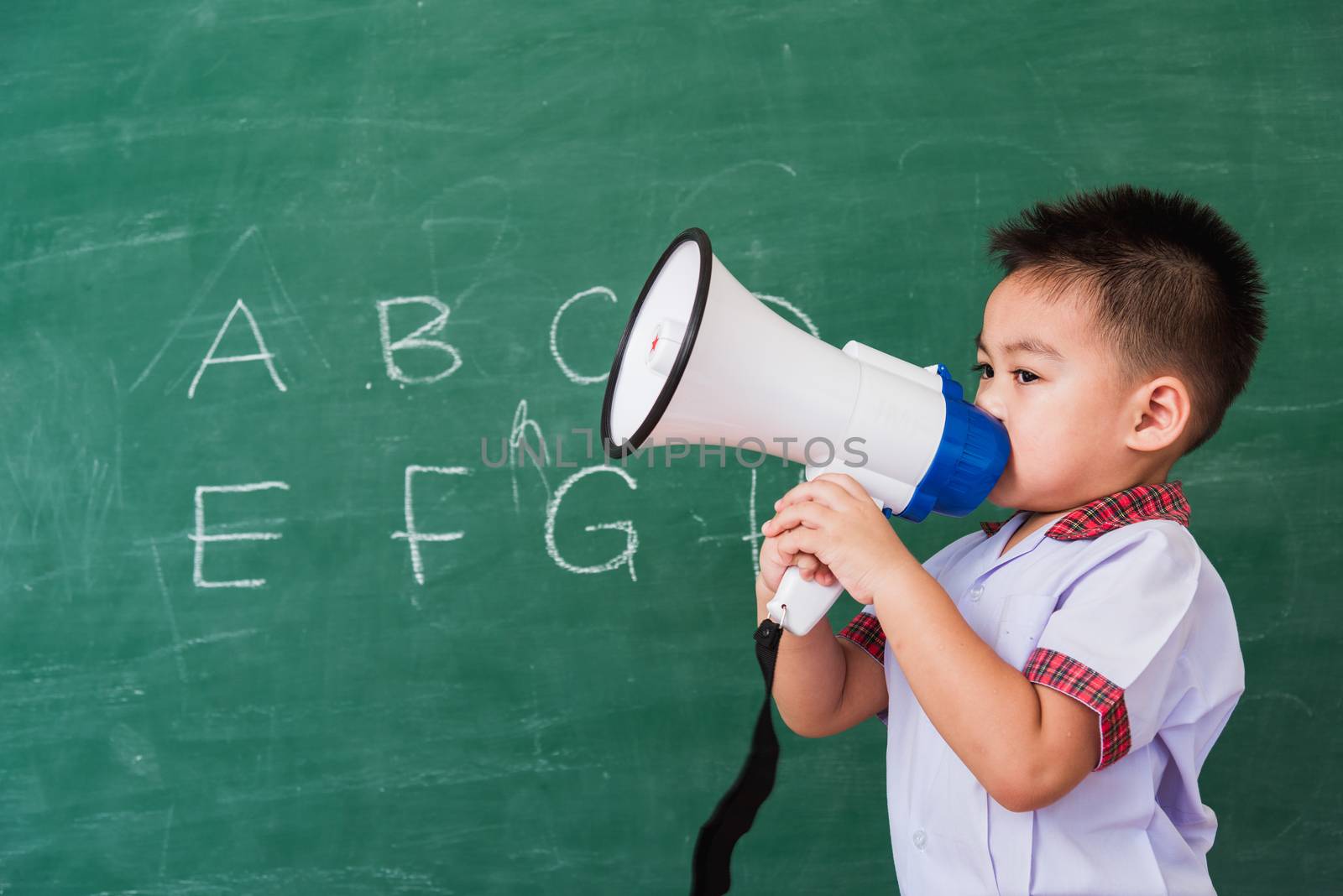 Back to School. Asian funny cute little child boy kindergarten preschool in student uniform speaking through megaphone against on green school blackboard, First time to school education concept