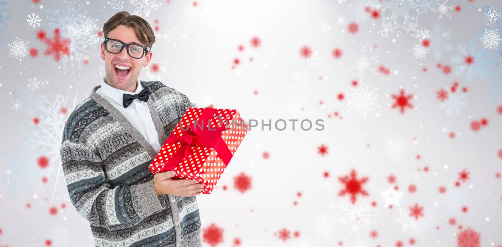Happy geeky hipster with wool jacket holding present  against snowflake pattern