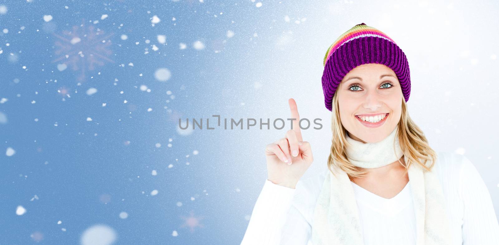 Joyful woman with a colorful hat pointing upwards against snow