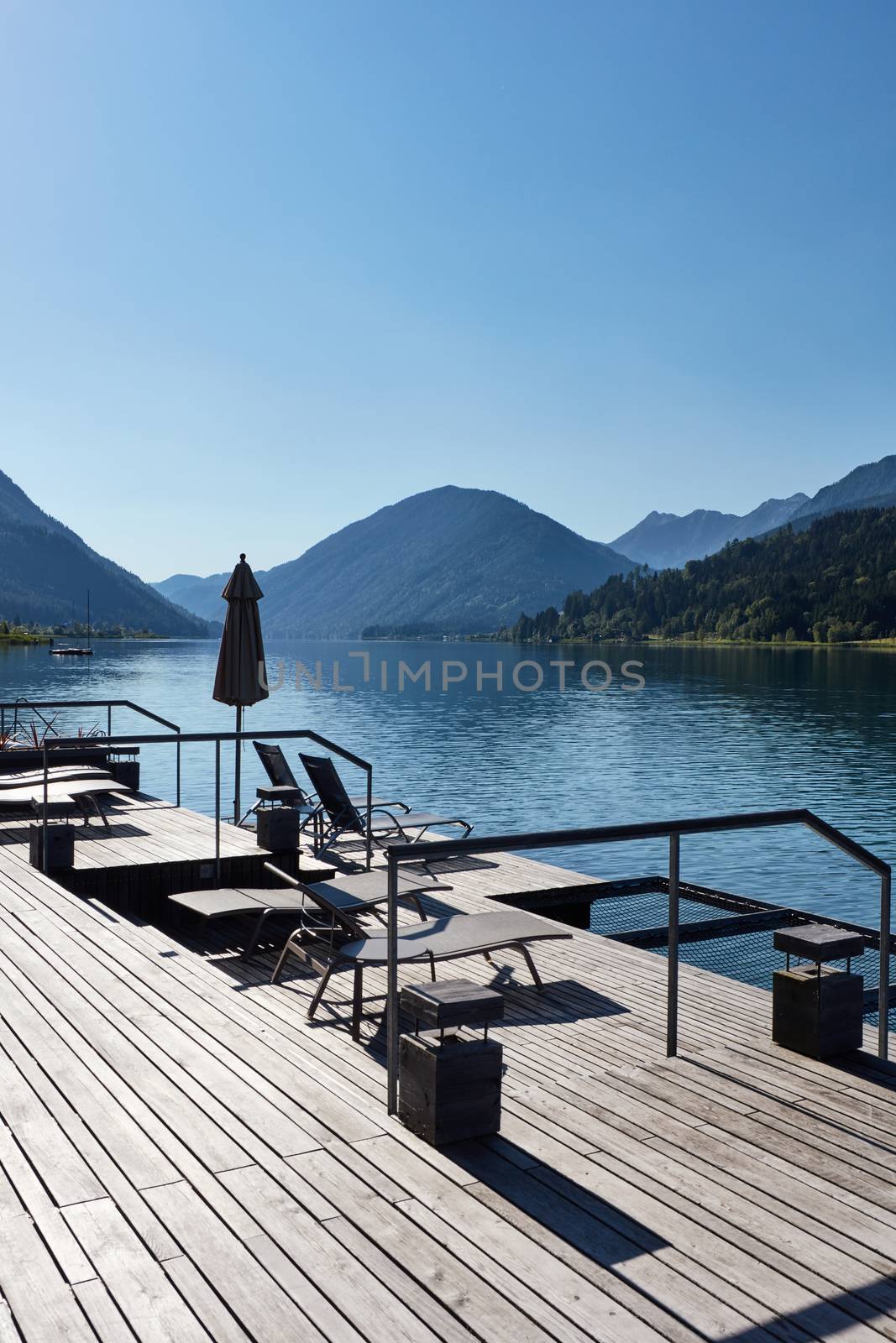 Hotel terrace with deck chairs on the shores of an alpine lake surrounded by mountains by ArturNyk