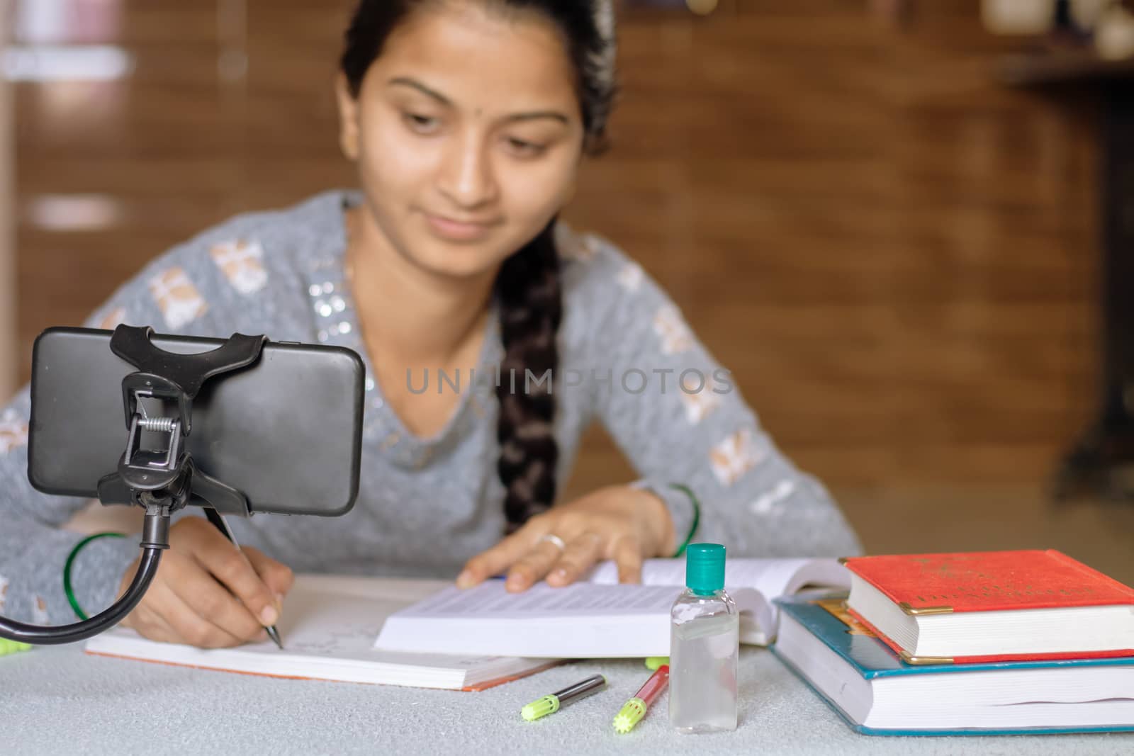 Selective focus of Mobile, Concept of e-learning at home due to covid-19 or coronavirus isolation - Young college girl taking notes by looking into virtual class on mobile due to isolation. by lakshmiprasad.maski@gmai.com