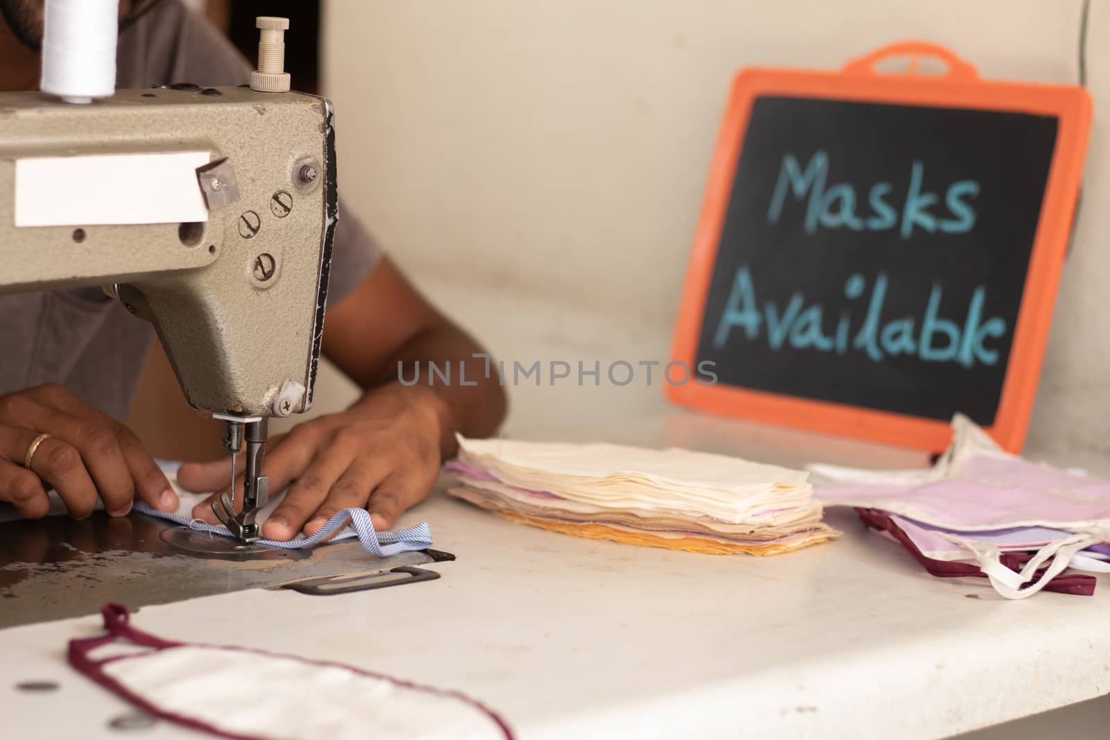 Small business of mask producing and selling at home in India due shortage of medical masks during covid-19 or coronavirus pandemic - Using Sewing machine to sew face mask with mask available board.