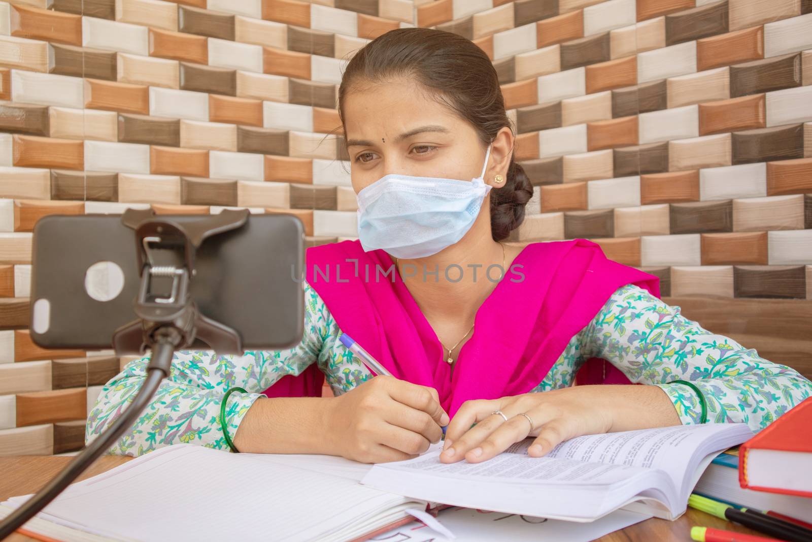 Concept of homeschooling and e-learning, College girl with medical mask listing virtual class on mobile during covid-19 or coronavirus pandemic lock down. by lakshmiprasad.maski@gmai.com