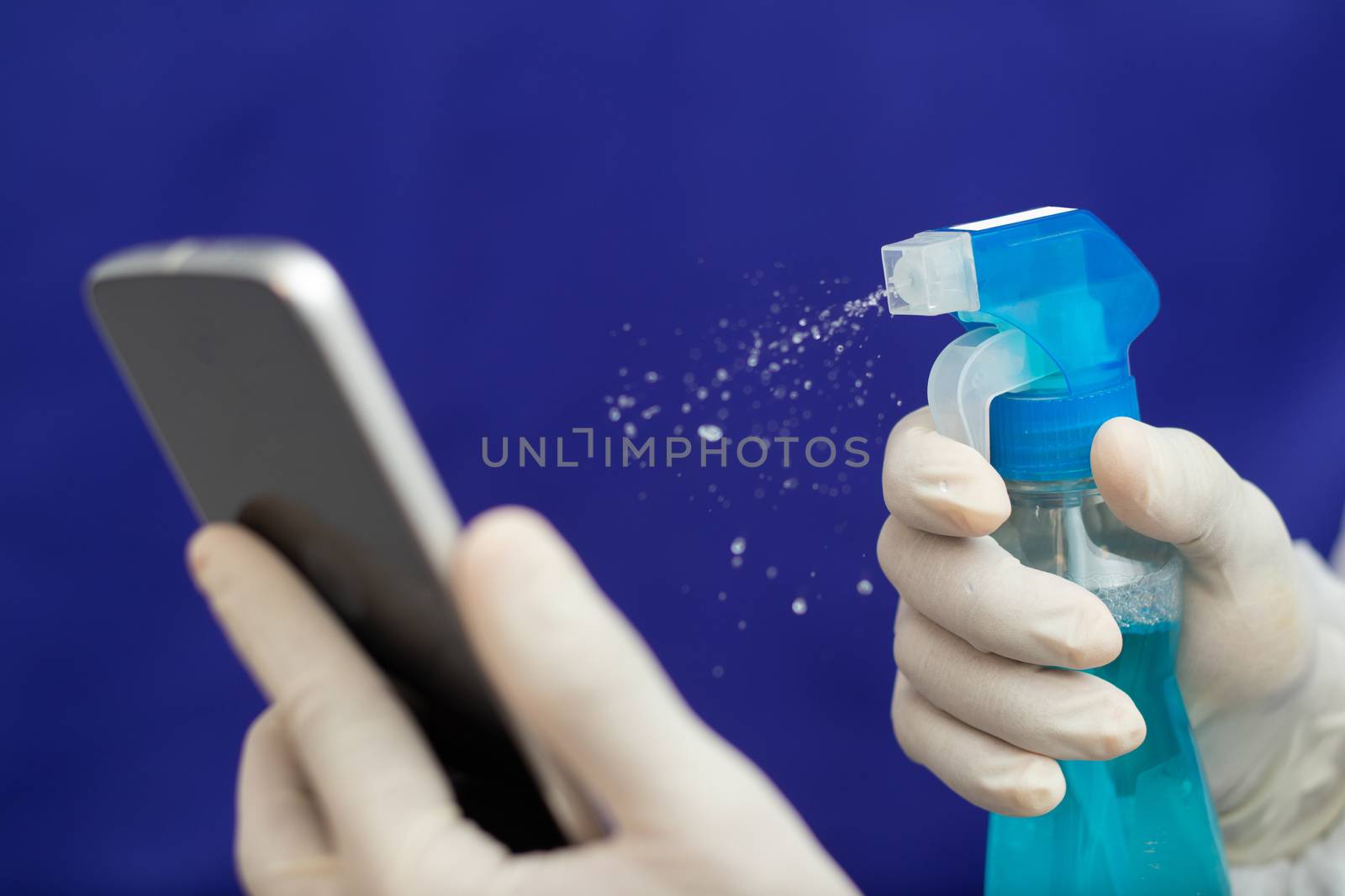 Doctor Cleaning mobile phone to eliminate Covid-19 - Nurse hands with gloves cleaning the phone by liquid sanitizer at hospital - alcohol to wipe contaminating with Coronavirus by lakshmiprasad.maski@gmai.com