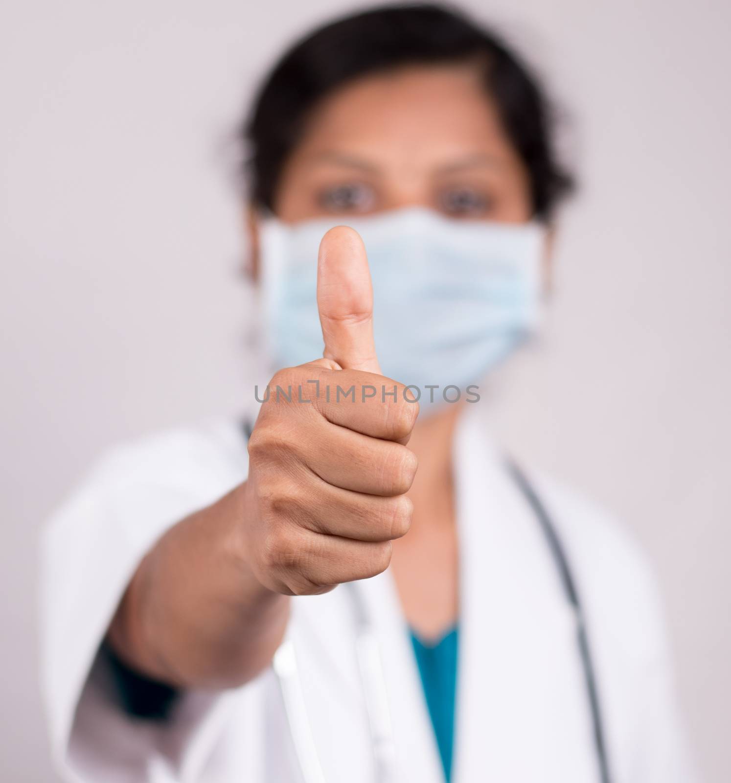 Woman doctor with medical mask in uniform showing thumbs up on isolated background - Concept of approval or ok by doctor during covid-19 or coronavirus pandemic