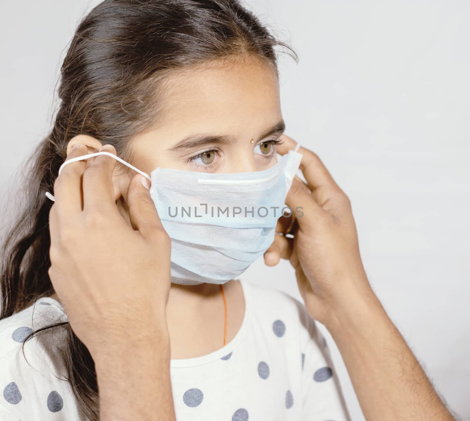 Prevention of spreading the coronavirus or COVID-19 outbreak by wearing mask - Father wearing a disposable hygienic face mask to his young girl daughter to protect spread of disease. by lakshmiprasad.maski@gmai.com