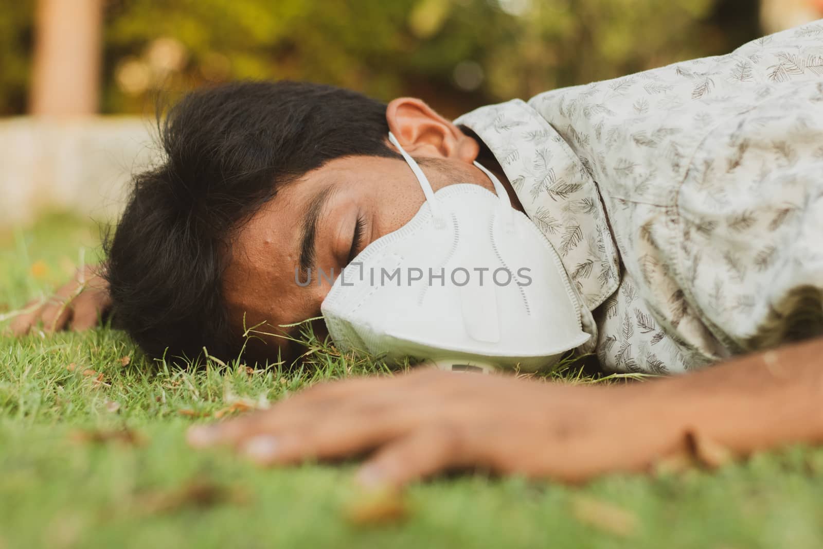 Sick young man fell down on ground with medical face mask - concept showing of sick, ill health, dehydration or sun stroke