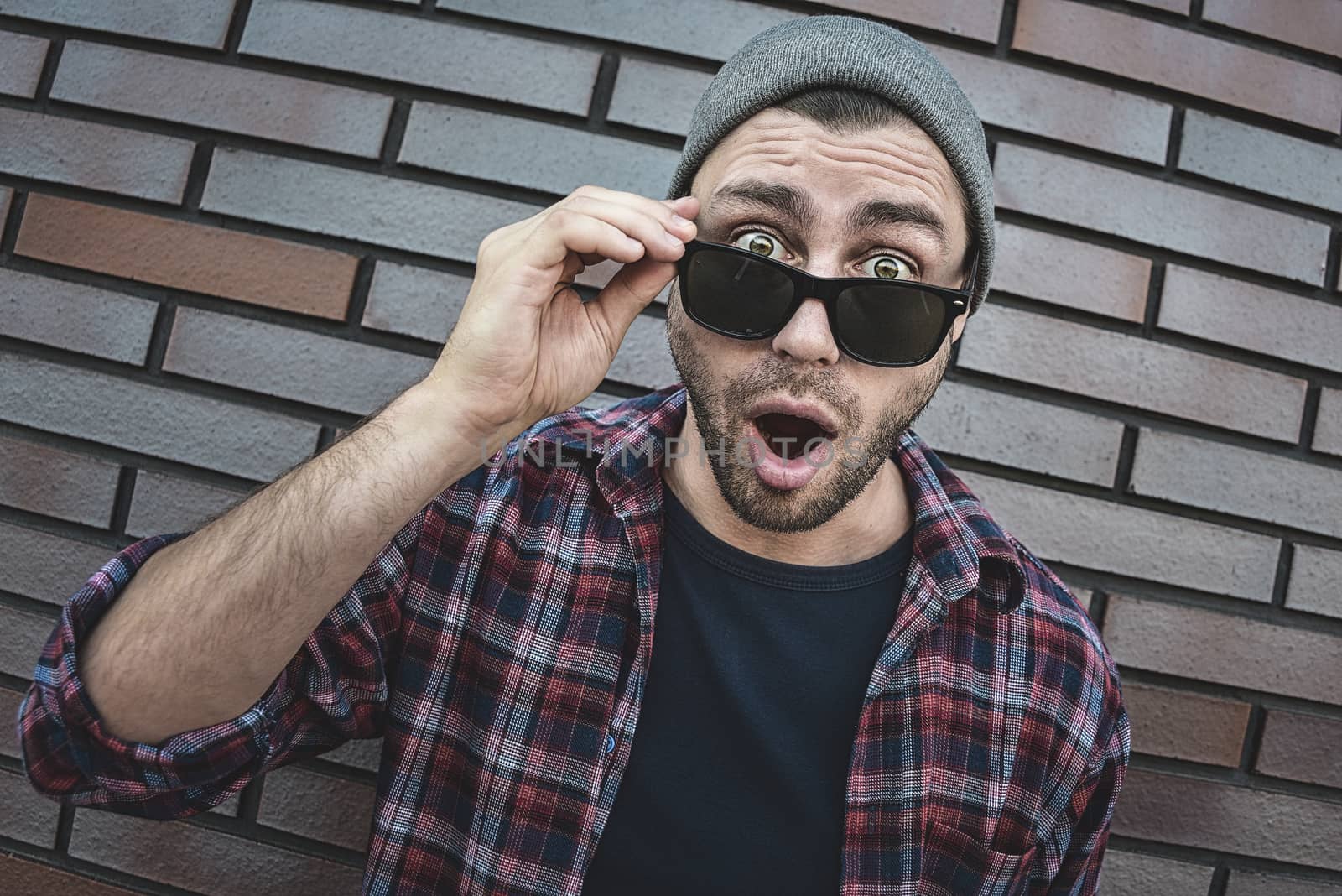 Shocked caucasian man in sunglasses standing at brick background.