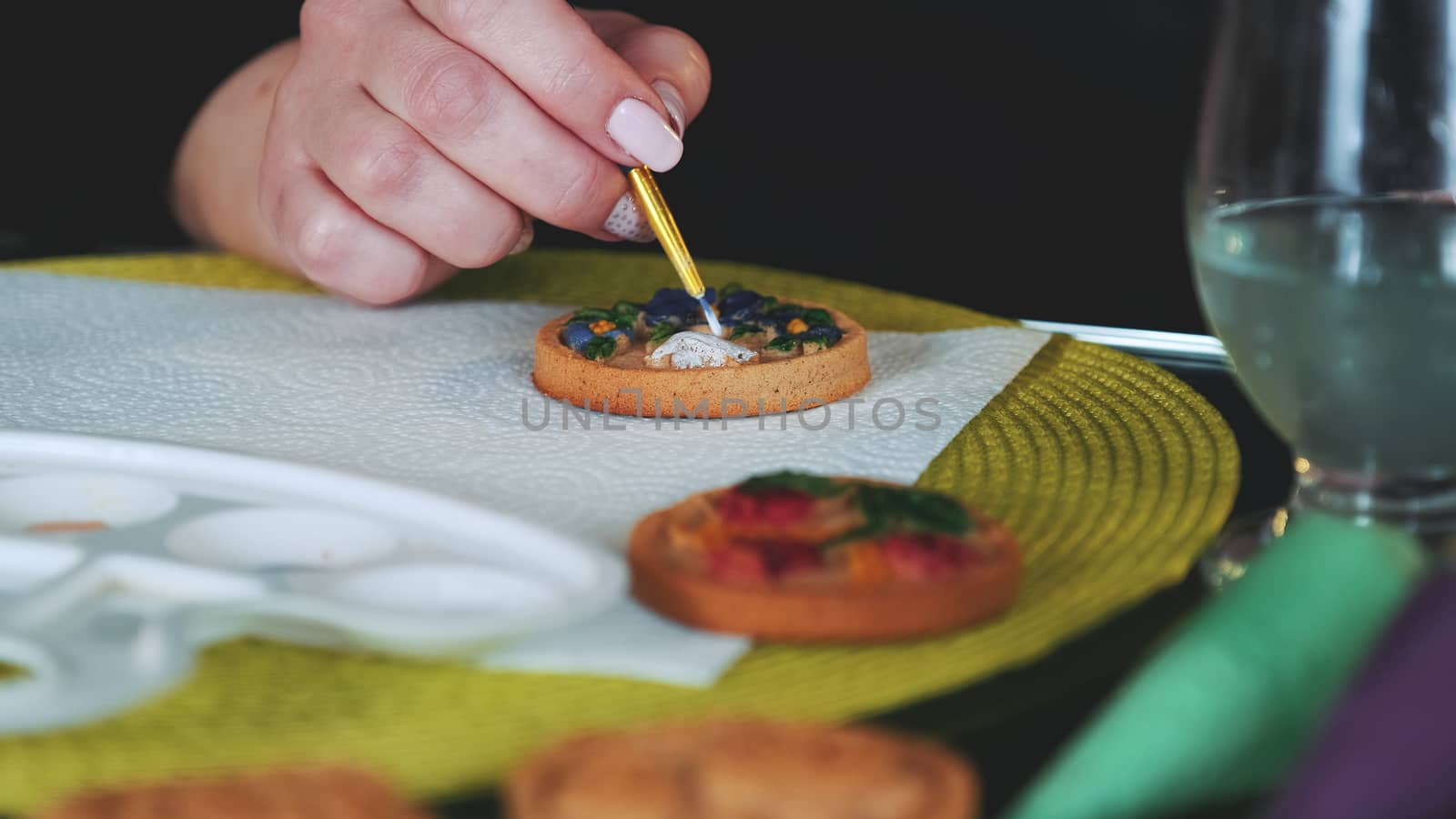 Cookies art decorating: woman painting cookies with brush and food colors on palette