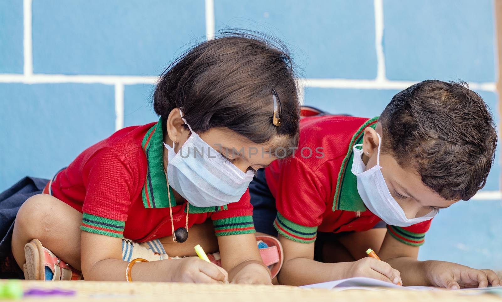 Kids busy in writing with medical face mask wearing due to covid-19 or coronavirus outbreak or pandemic at school - children painting at home during lockdown. by lakshmiprasad.maski@gmai.com