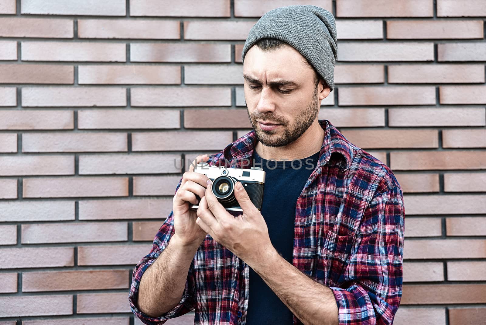 Man with retro photo camera Fashion Travel Lifestyle outdoor while standing against brick wall background.