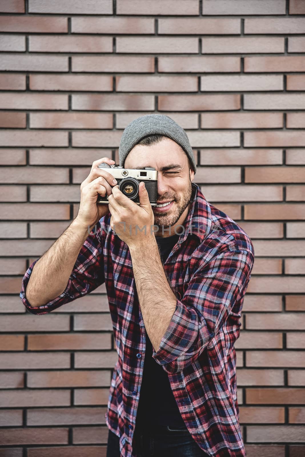 Man with retro photo camera Fashion Travel Lifestyle outdoor while standing against brick wall background.