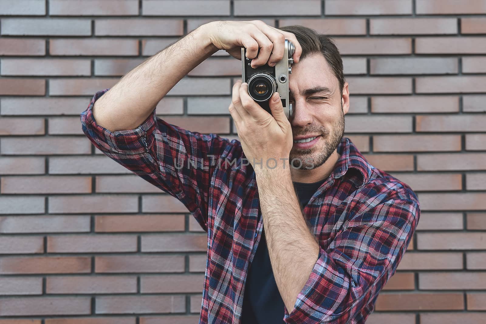 Man with retro photo camera Fashion Travel Lifestyle outdoor while standing against brick wall background.