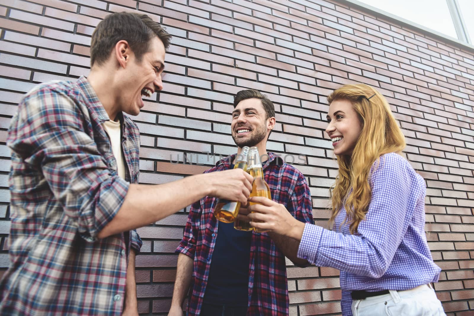 The three happy friends enjoying with beer on a brown brick wall background.