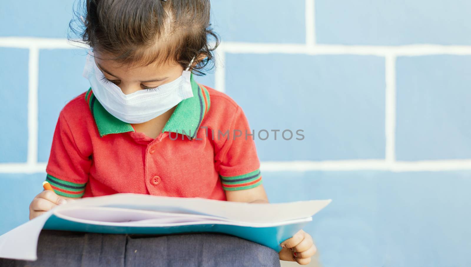 Covid 19 or Coronavirus and Air pollution pm2.5 concept - Little girl wearing medical mask and busy in writing at school - showing Wuhan covid-19 or sars cov 19 outbreak or epidemic of virus. by lakshmiprasad.maski@gmai.com