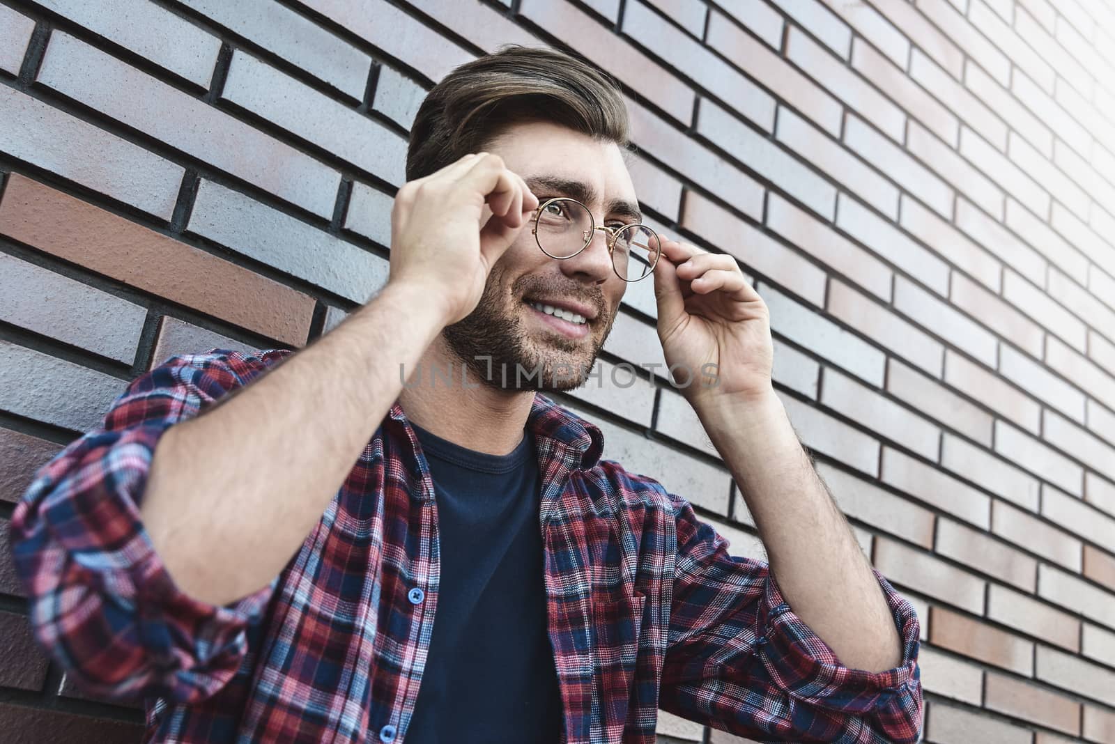 Portrait of smiling handsome man in round glasses and shirt isolated on brown brick wall