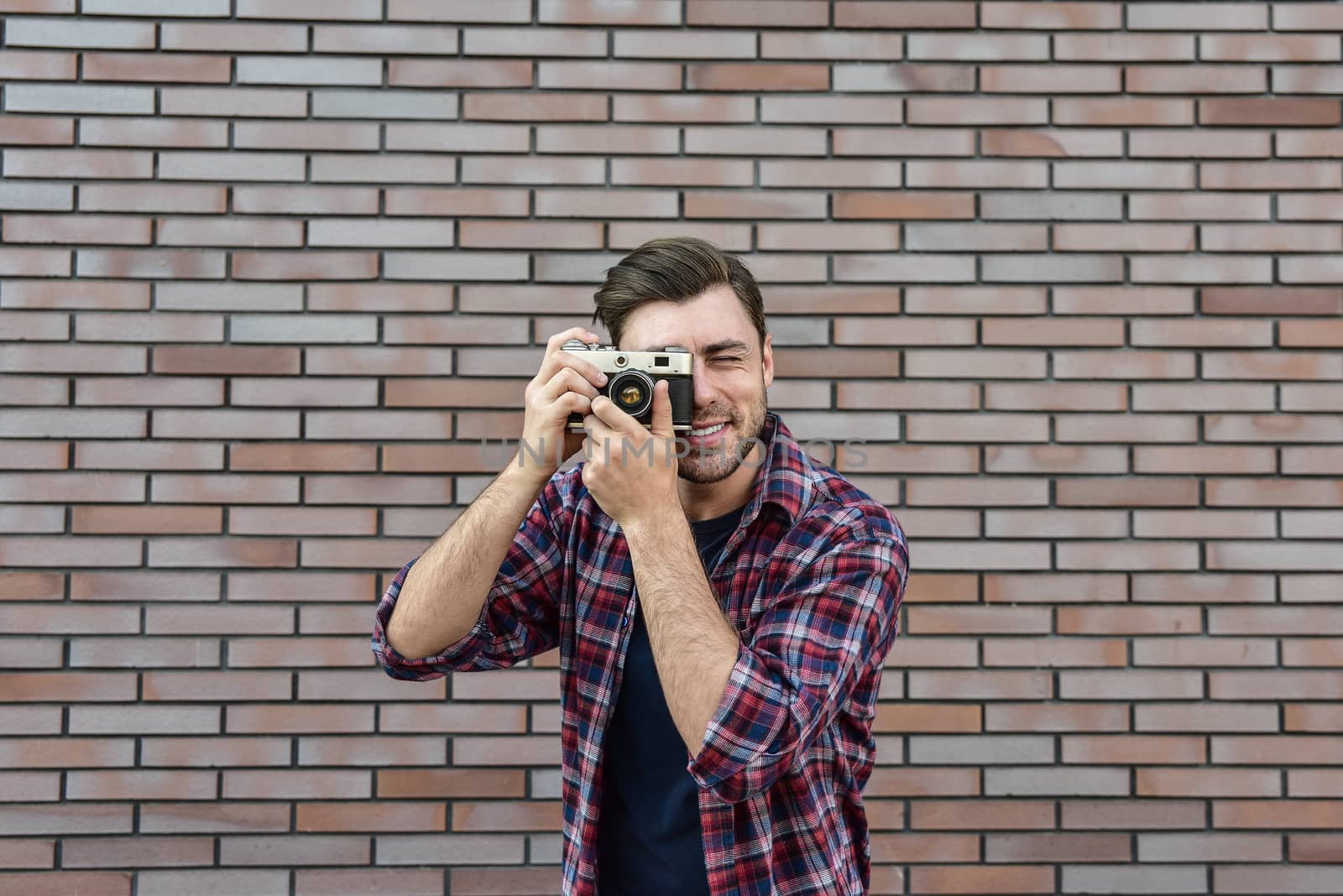 Man with retro photo camera Fashion Travel Lifestyle outdoor while standing against brick wall background.