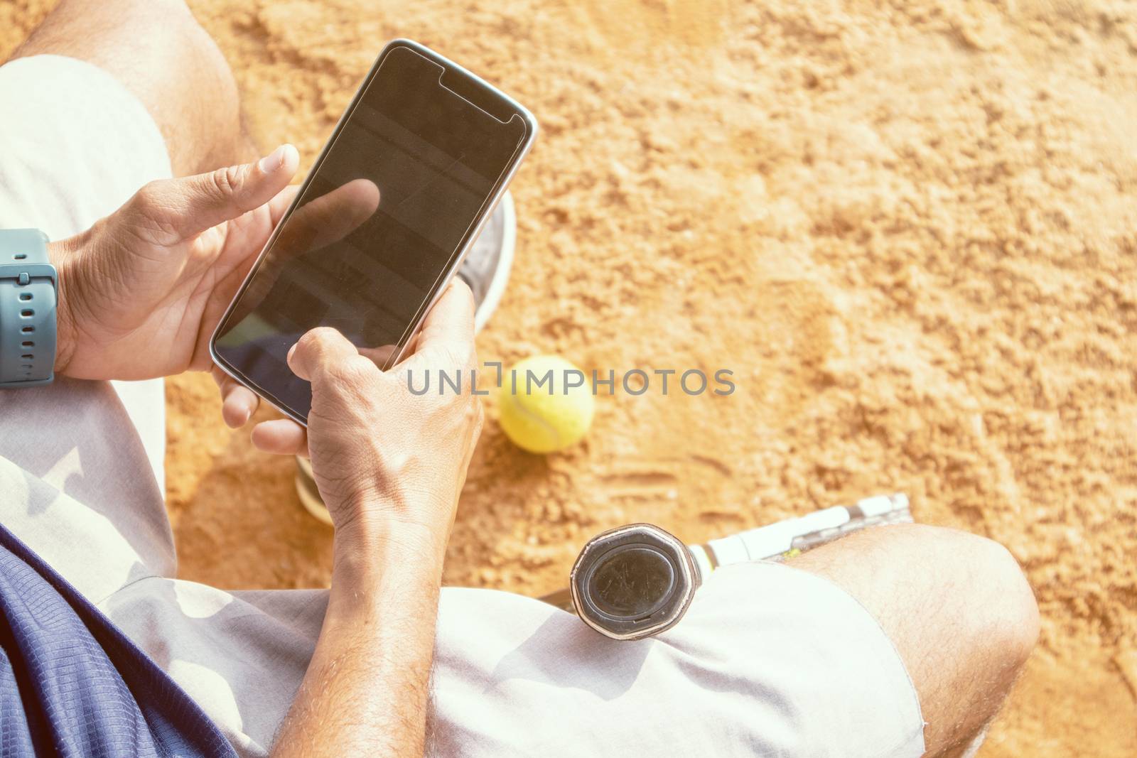 High angle shot of young tennis player taking rest after training and busy in using mobile phone - fitness, Sport and recreation concept.