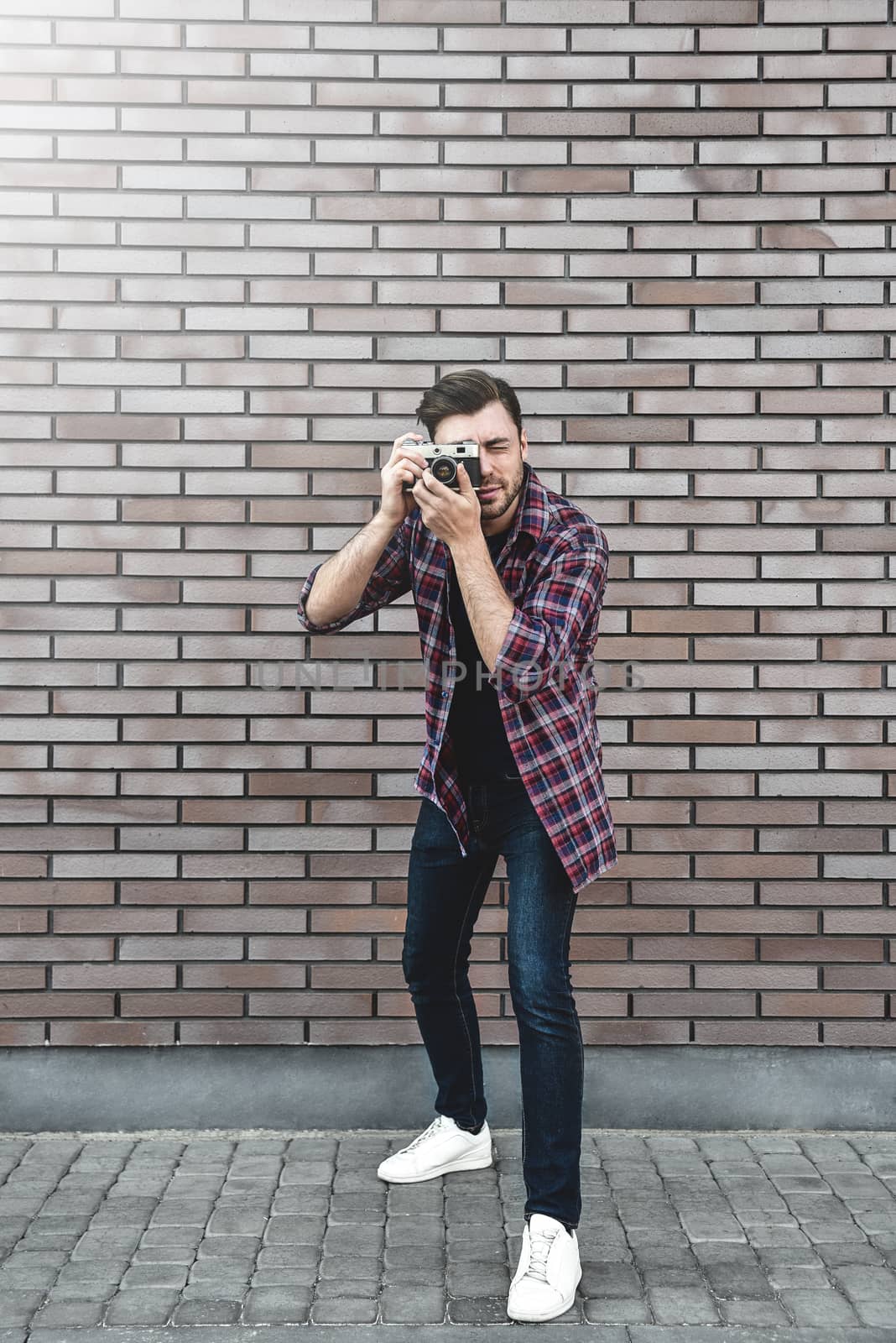 Man with retro photo camera Fashion Travel Lifestyle outdoor while standing against brick wall background.