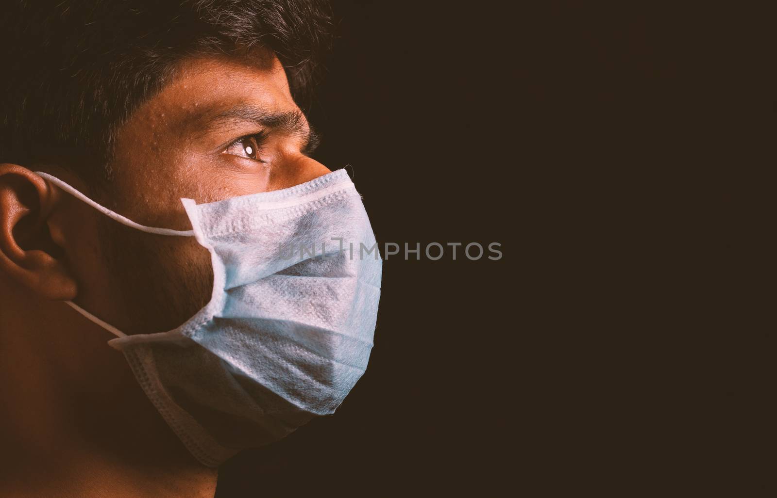 Young man wearing medical face mask to protect from spreading coronavirus outbreak infection in dark room and thinking of virus attack