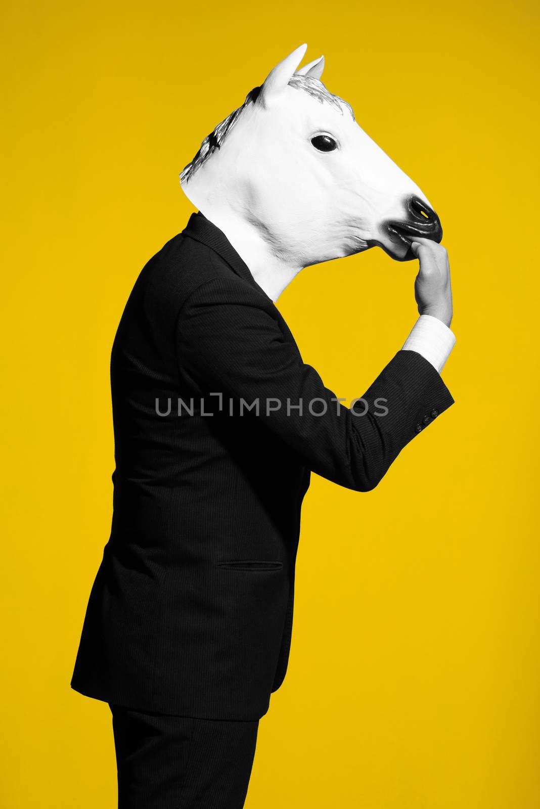 A man in a suit and a horse mask bites own hand. Conceptual business background