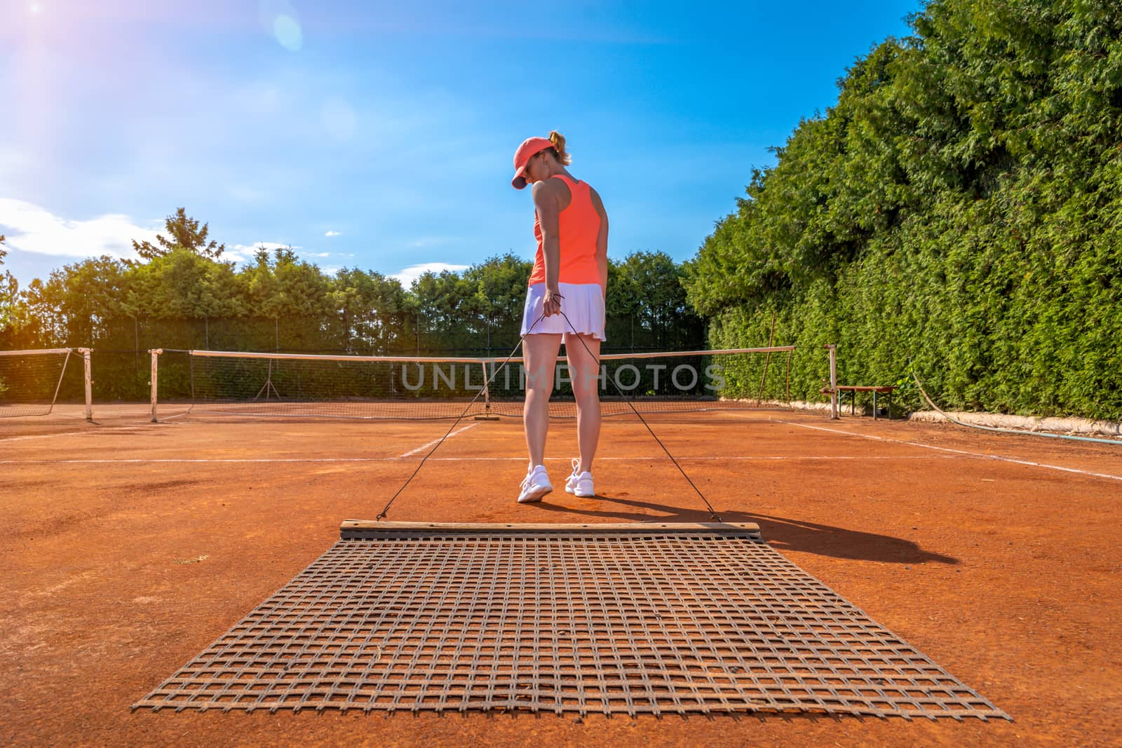 sweeping orange clay on an outdoor tennis court. young woman by Edophoto