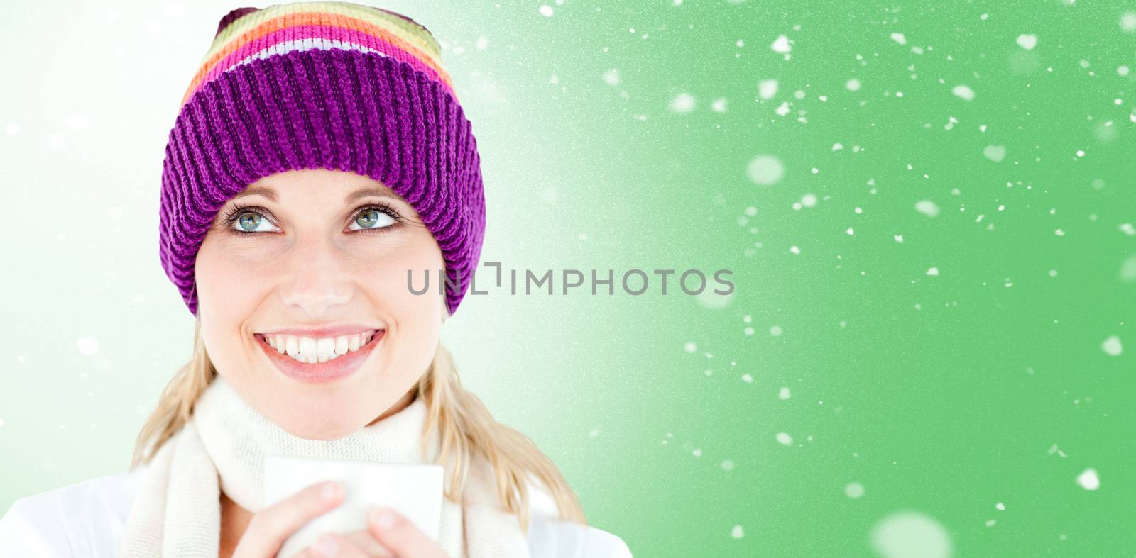 Smiling woman with a colorful hat and a cup in her hands against snow