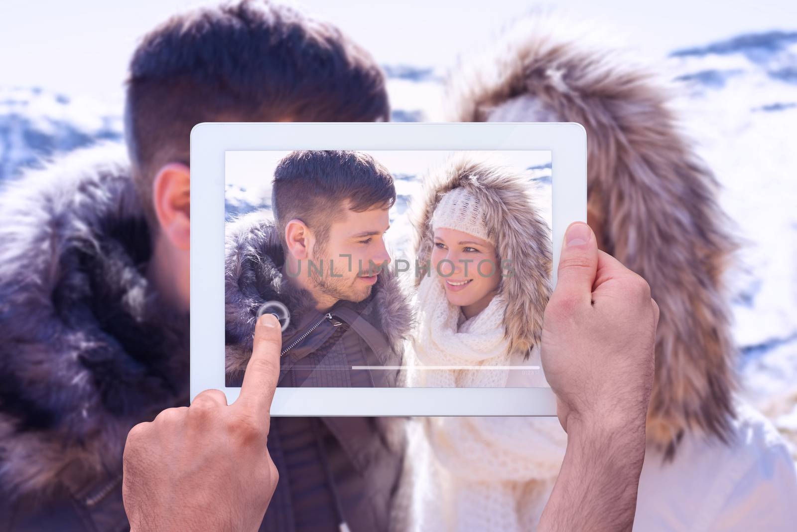 Hand holding tablet pc against couple in fur hood jackets against snowed mountain