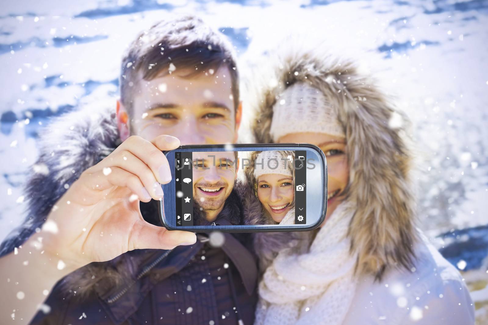 Hand holding smartphone showing against couple in fur hood jackets against snowed mountain range