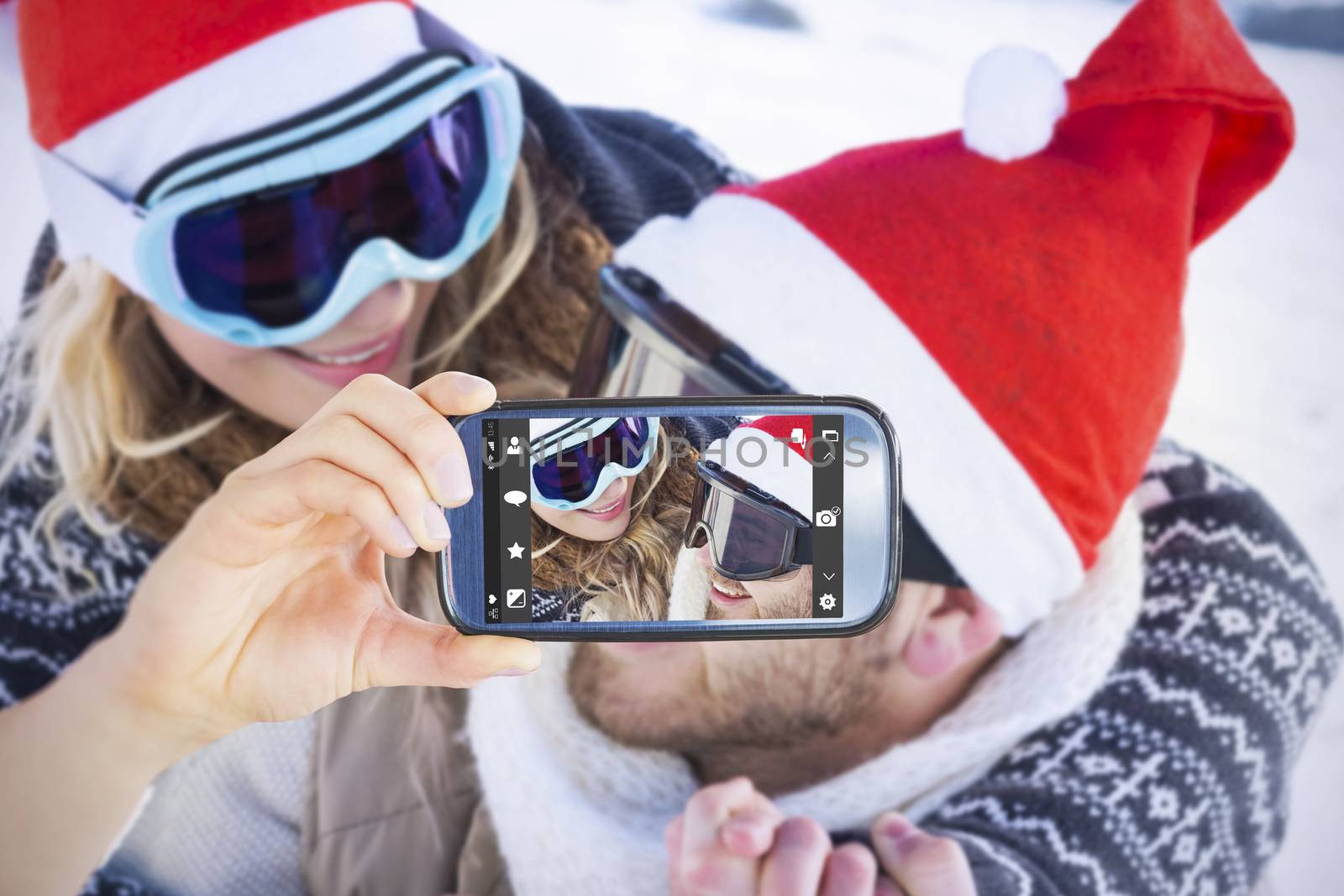 Hand holding smartphone showing against close up of a cheerful couple in ski goggles on snow