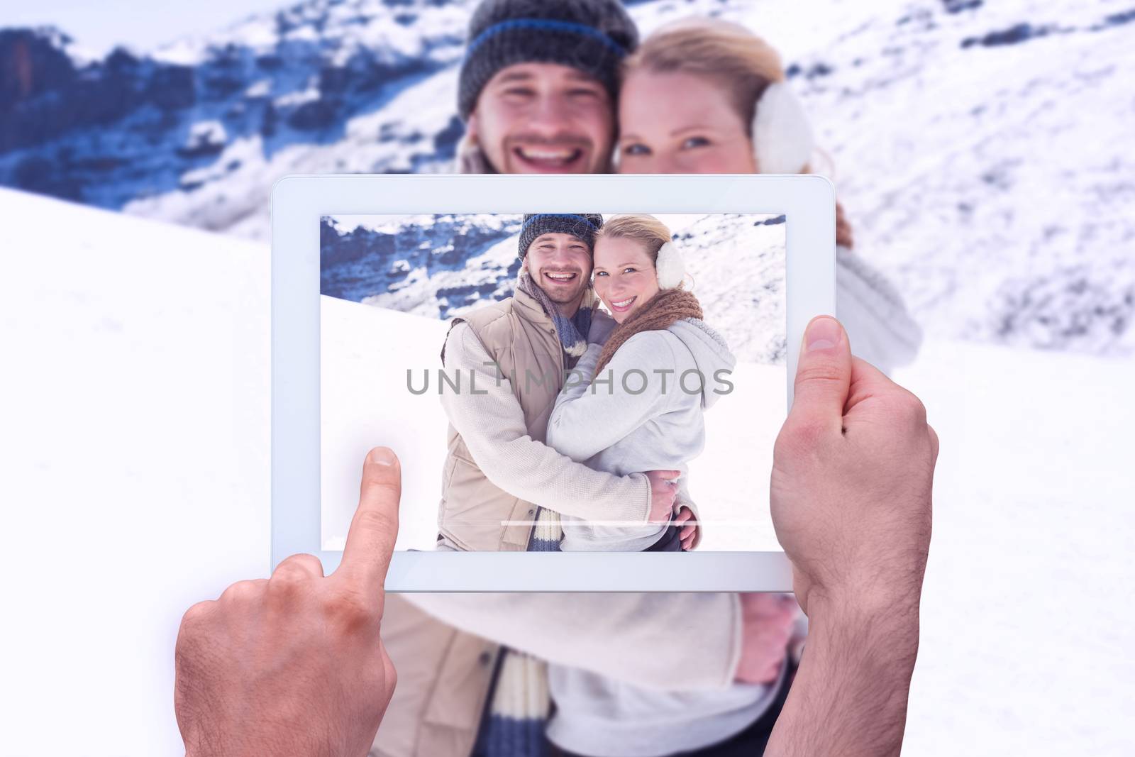 Hand holding tablet pc against loving couple in warm clothing on snowed landscape