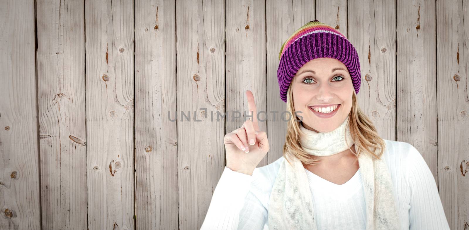 Joyful woman with a colorful hat pointing upwards against wooden background