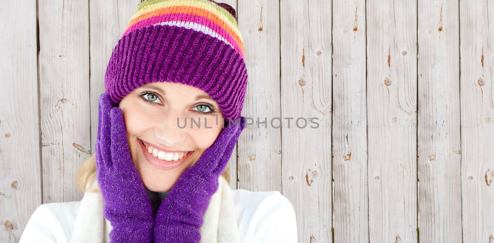 Radiant young woman with cap and gloves in the winter against wooden background