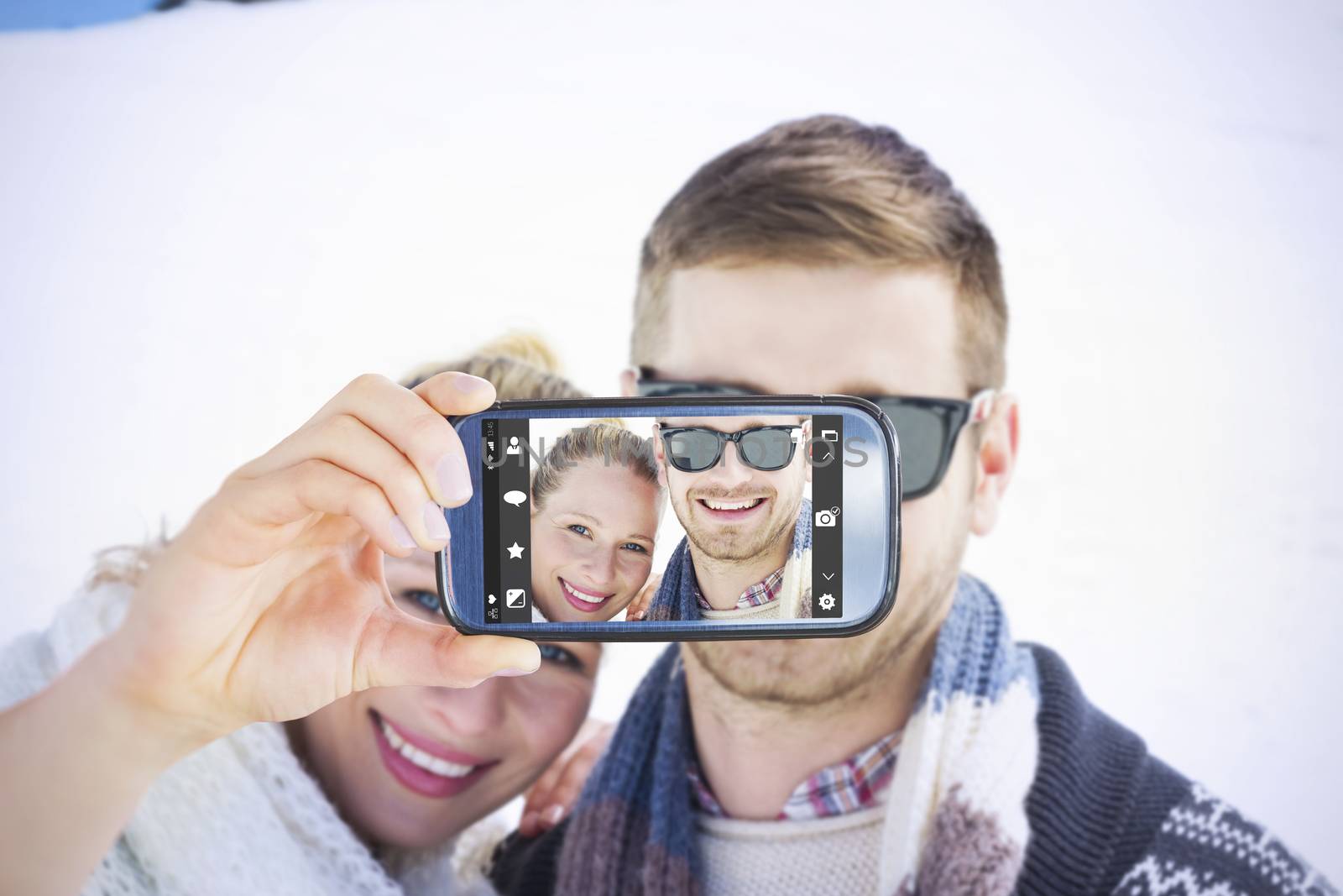 Hand holding smartphone showing against smiling couple in front of snowed hill