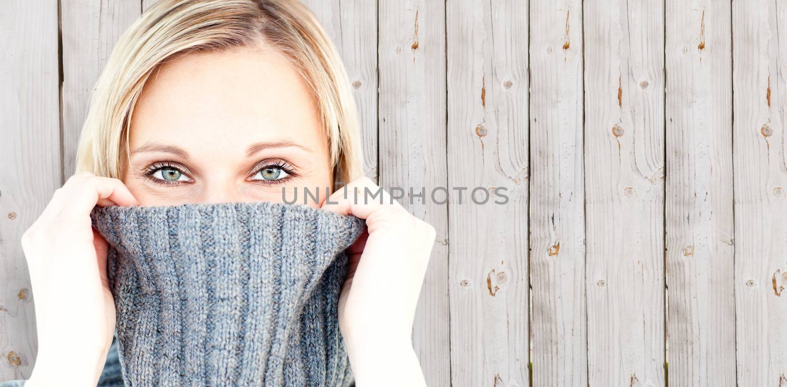 Delighted woman wearing a poloneck-sweater smiling at the camera against wooden background