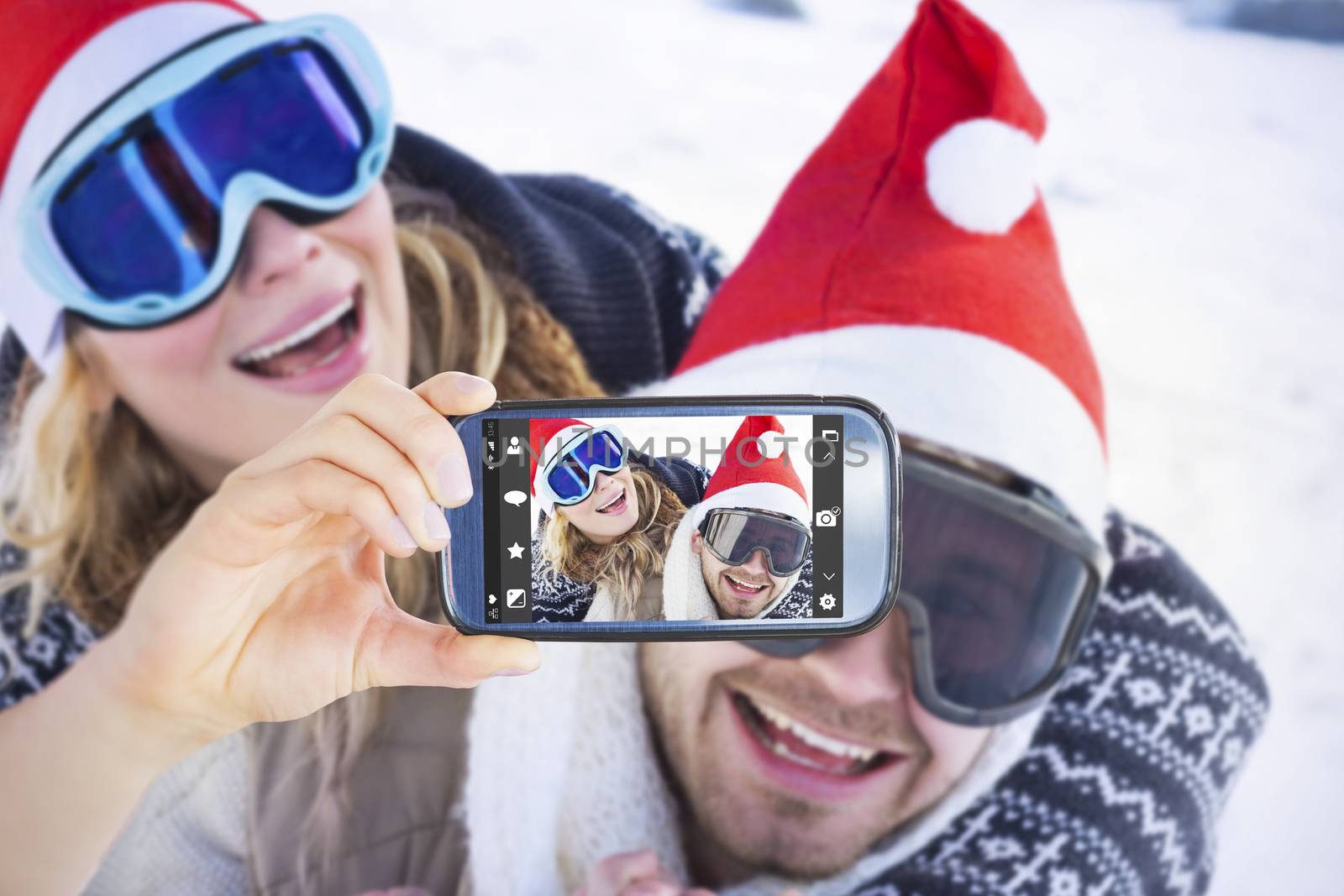 Hand holding smartphone showing against close up of a cheerful couple in ski goggles on snow
