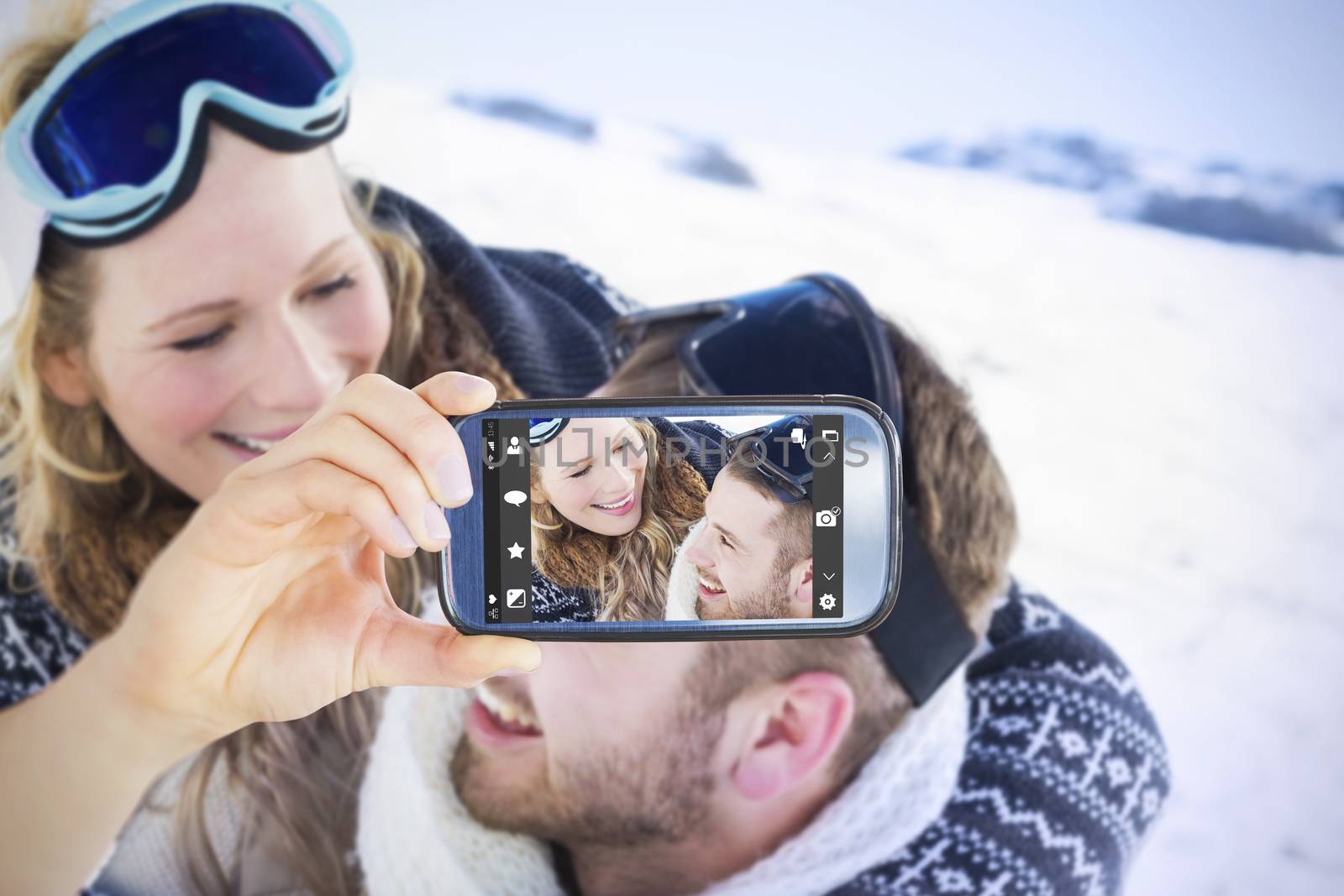 Hand holding smartphone showing against close up of a cheerful couple with ski goggles on snow
