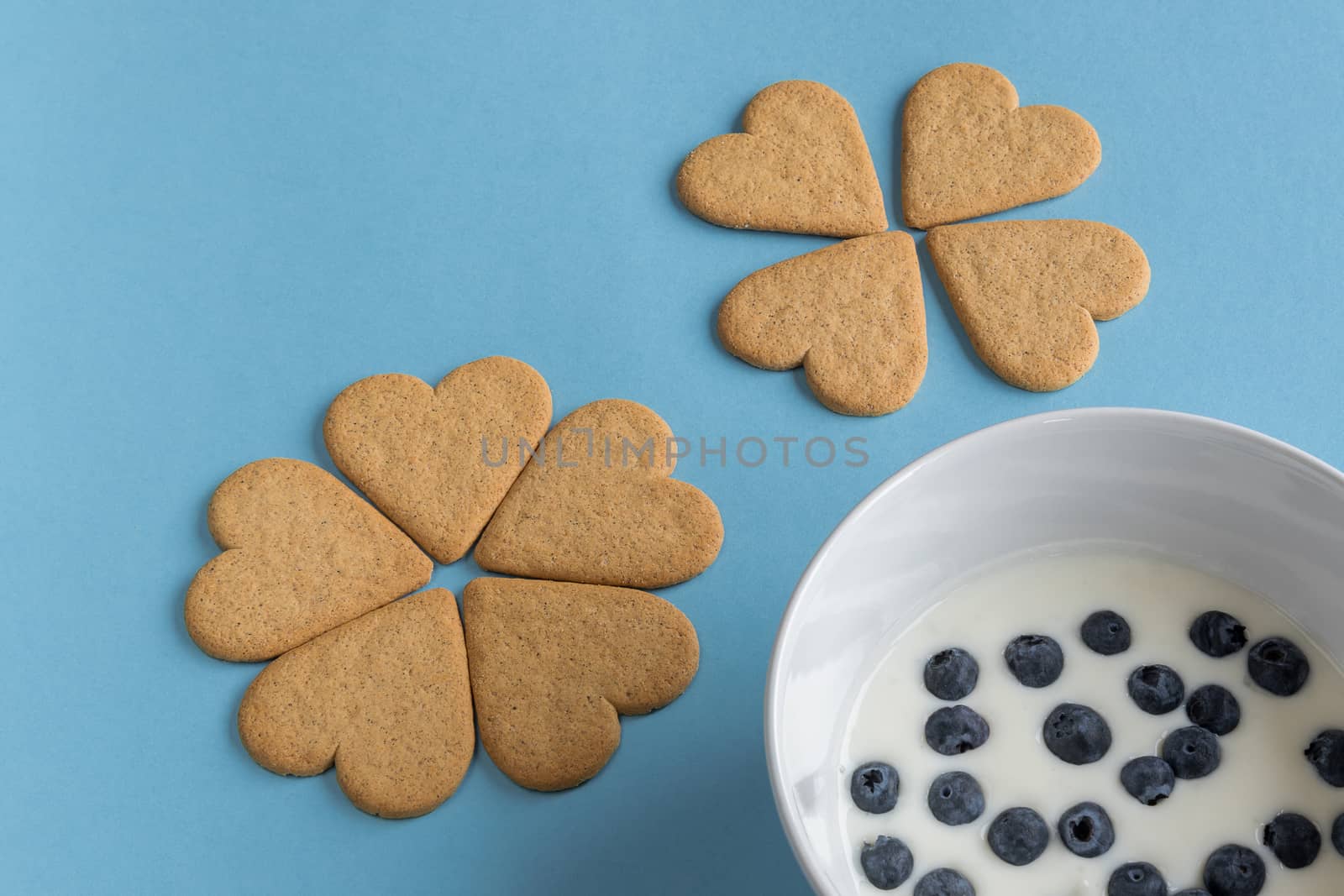 Breakfast. Close-up of heart shaped cookies like a flower petals. A bowl of yogurt with blueberries. Light blue background. Copy space.