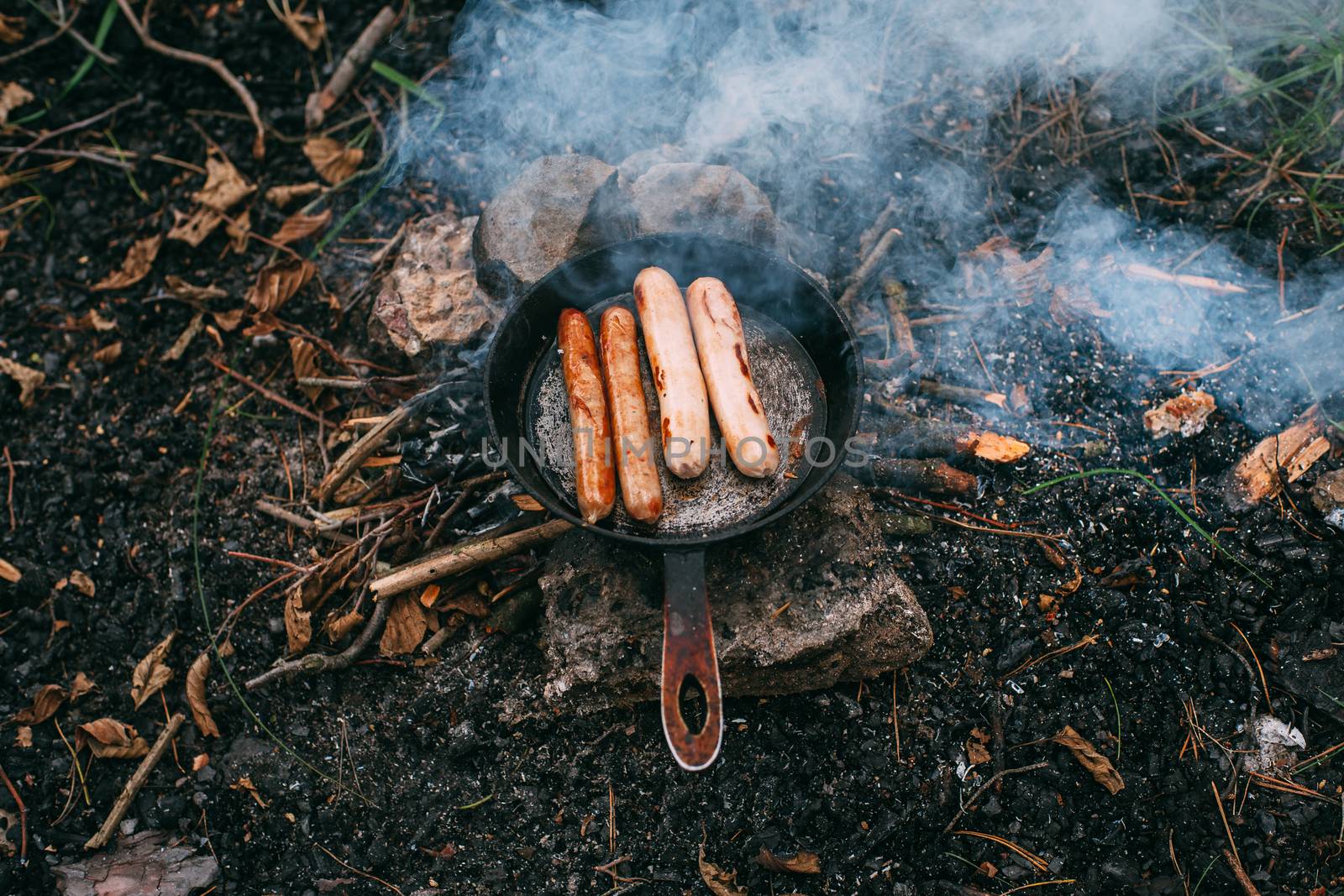 Roasting sausages in a frying pan over an open fire. Preparing food in nature. Lunch in the open air. Picnic in the forest. Food on fire