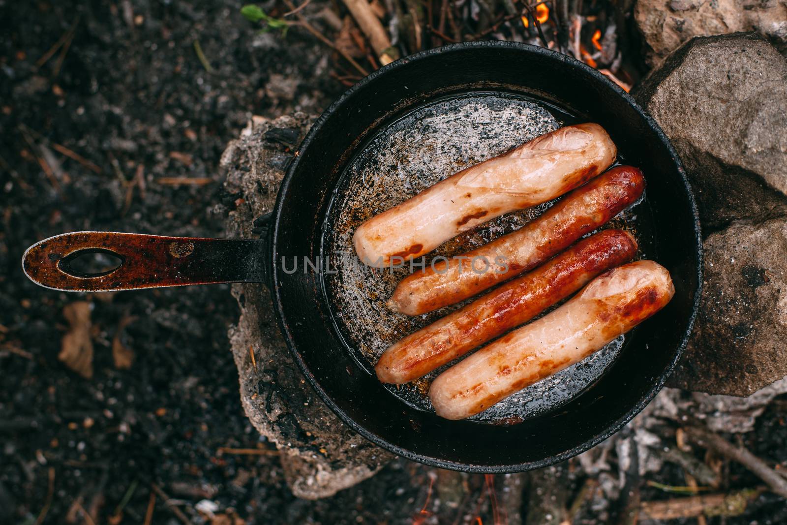 Roasting sausages in a frying pan over an open fire. Preparing food in nature. Lunch in the open air. Picnic in the forest. Food on fire