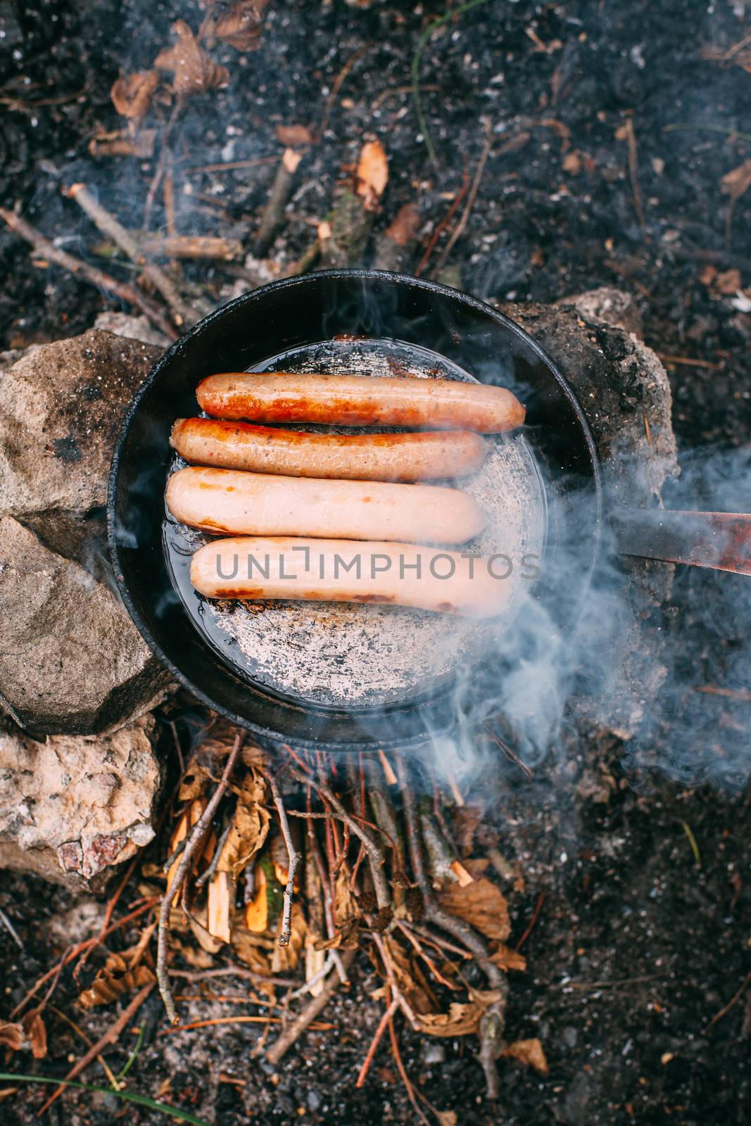 Roasting sausages in a frying pan over an open fire. Preparing f by Opikanets