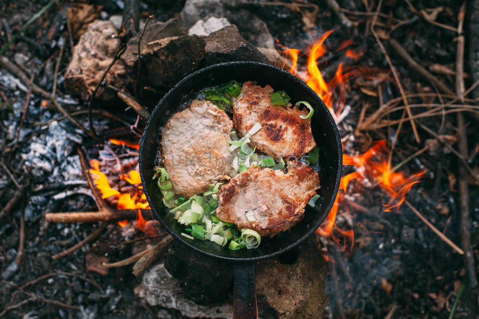 Frying meat in a pan over an open fire with leek. Steak in a pan on a fire. Cooking in nature. Picnic. Grill on fire.