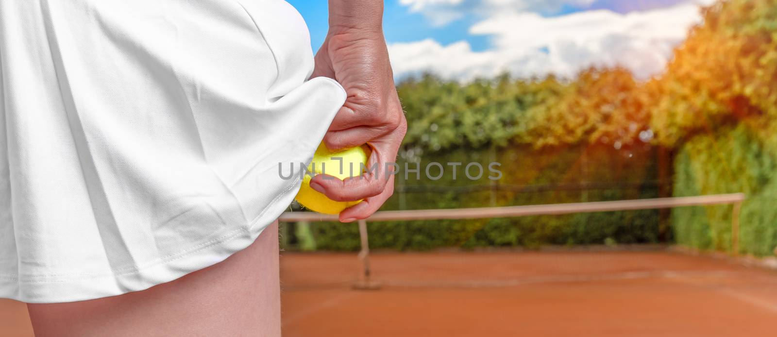 tennis ball in a womans hand in a skirt on a tennis court. preparation for serving a balloon in tennis. banner with copy space by Edophoto