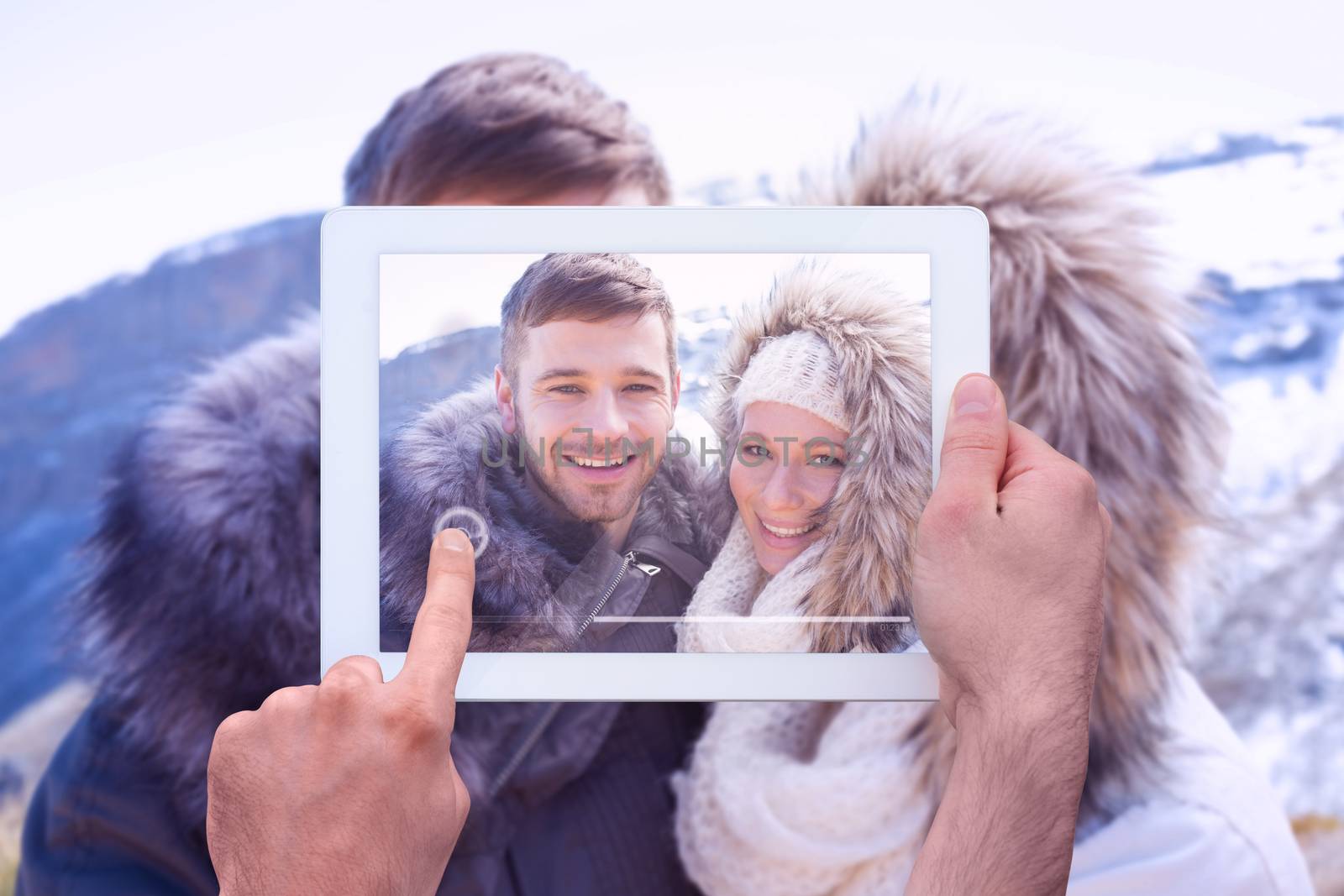 Hand holding tablet pc against loving couple in jackets against snowed mountain
