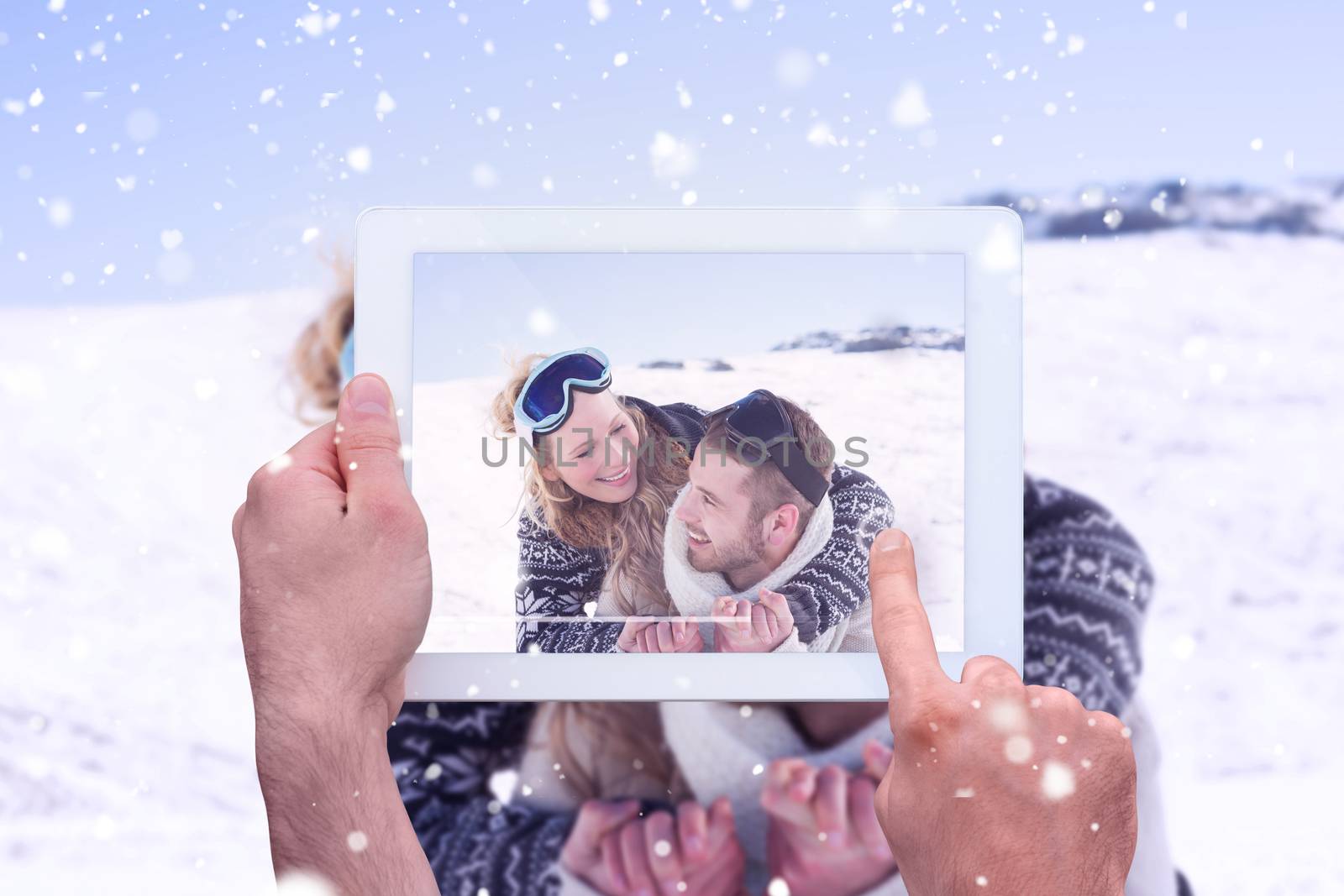 Hand holding tablet pc against close up of a cheerful couple with ski goggles on snow