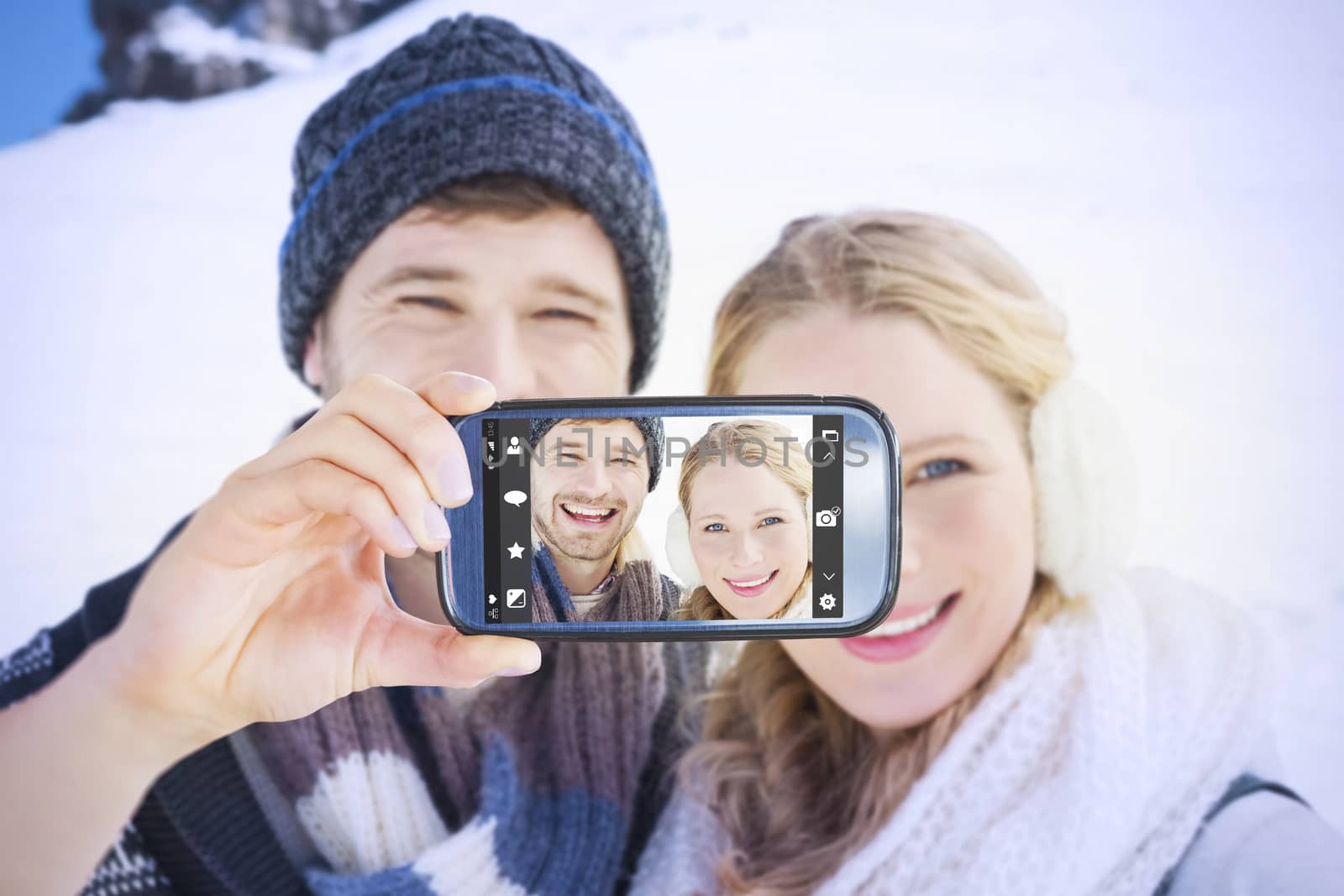 Hand holding smartphone showing against couple in front of snowed hill and clear blue sky