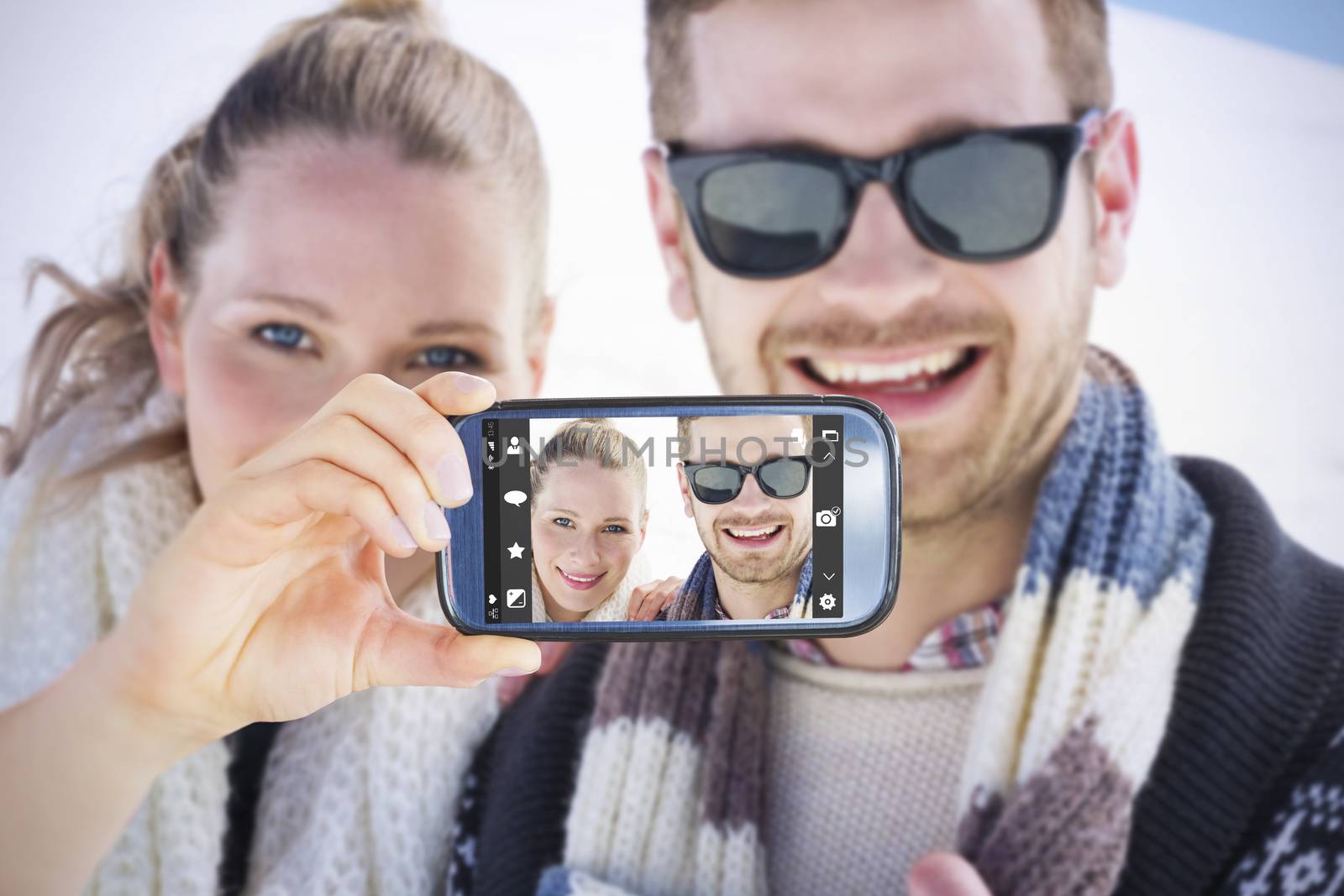 Hand holding smartphone showing against smiling couple in warm clothing on snow covered landscape