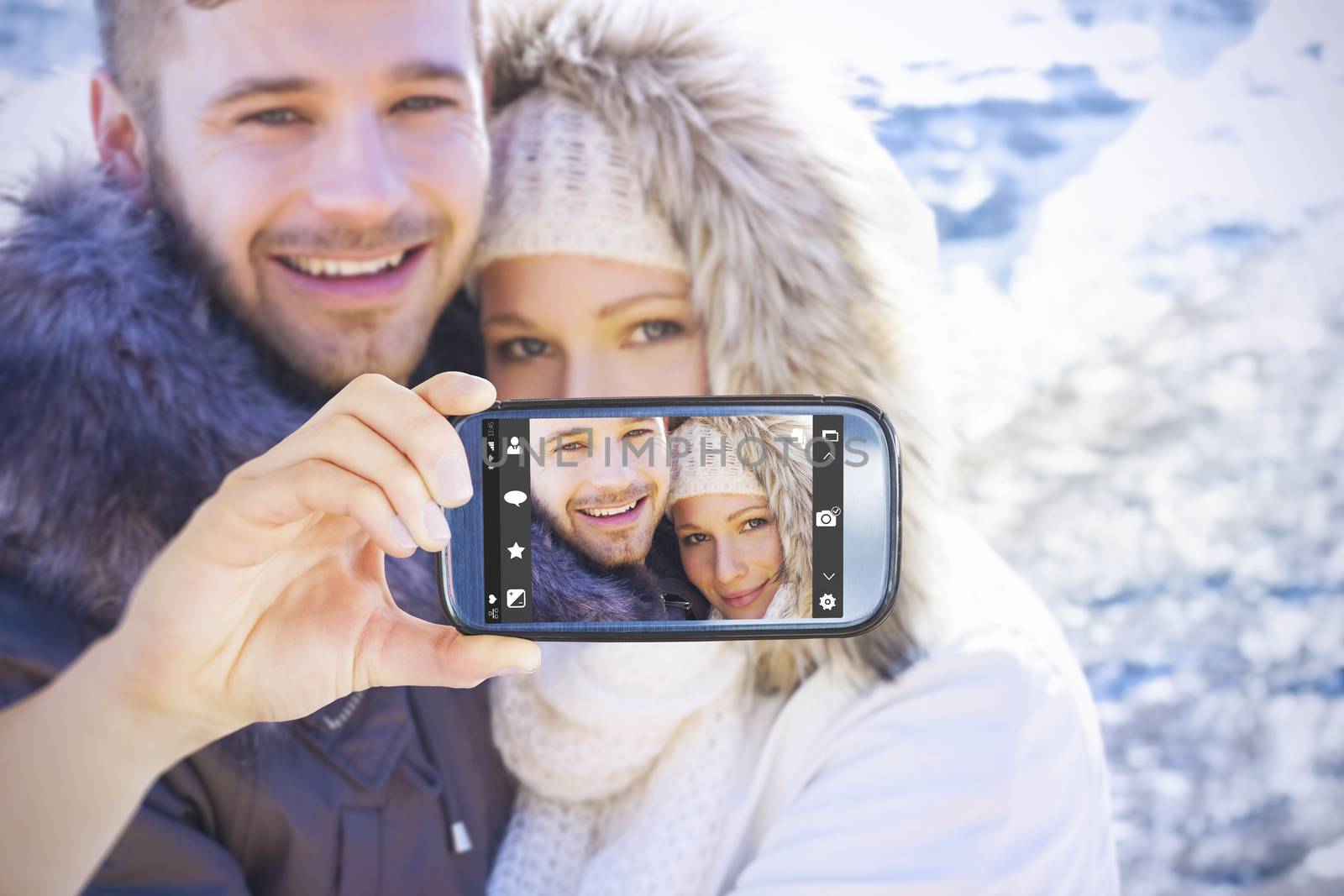Hand holding smartphone showing against couple in jackets embracing against snowed mountain