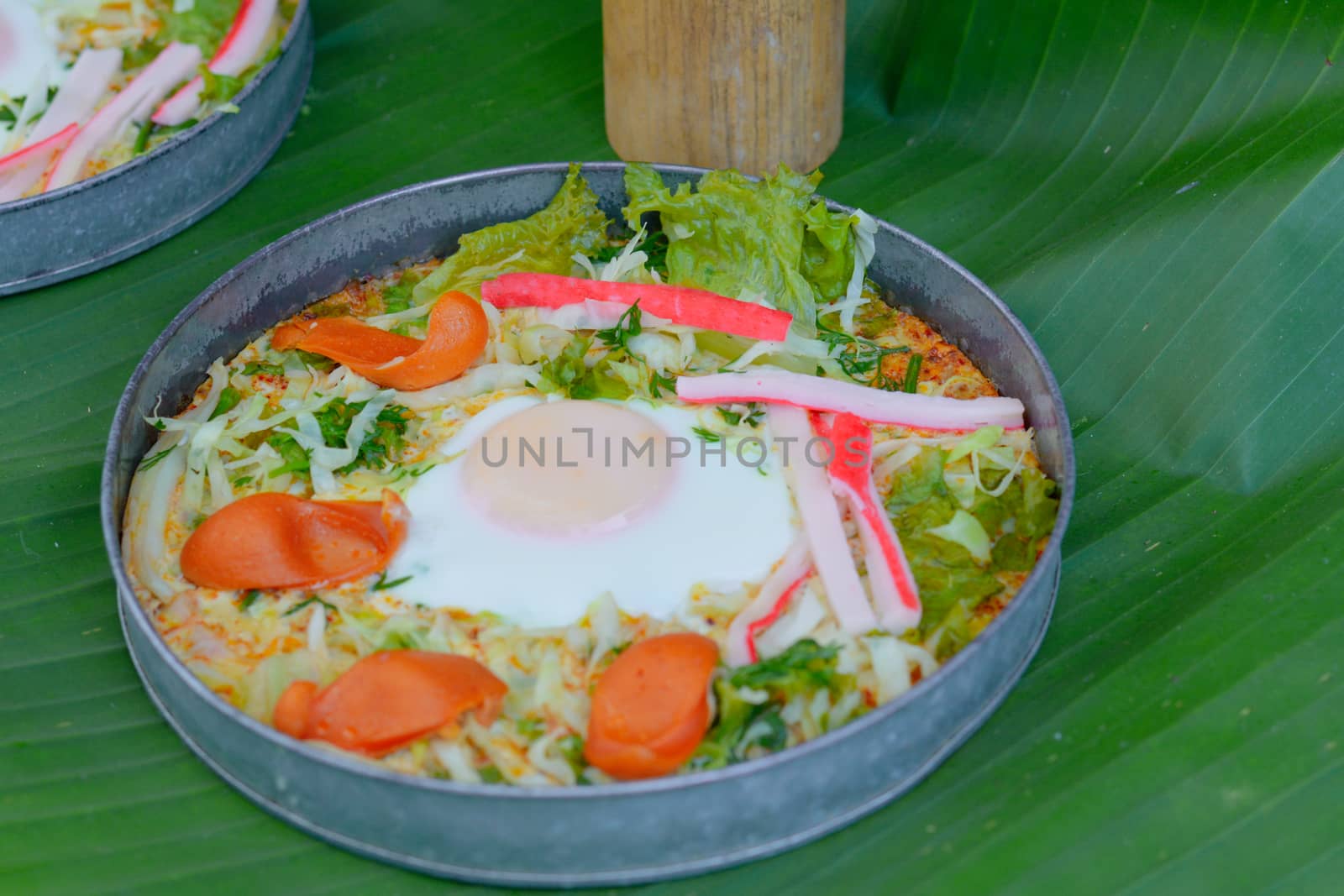 Delicious egg pan with sausage ,crab stick, cabbage and lettuce in small metal pan on green banana leave. Healthy breakfast in morning.